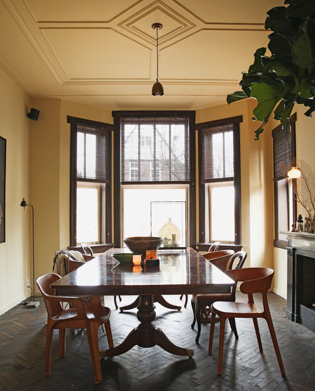 Vloer en kozijnen bruin gelakt. Antieke tafel. Met leer overtrokken plastic tuinstoel en vloerlamp van Brecht Murré Atelier. Overige stoelen kringloop en Marktplaats. De verlichting boven tafel is een tijdelijke oplossing: ‘We zoeken nog een kroonluchter of monumentale hanglamp.’ Verf muur en plafond F3.09.75 van Histor. Schalen Brecht Murré Atelier, Mobilia en Household Hardware.