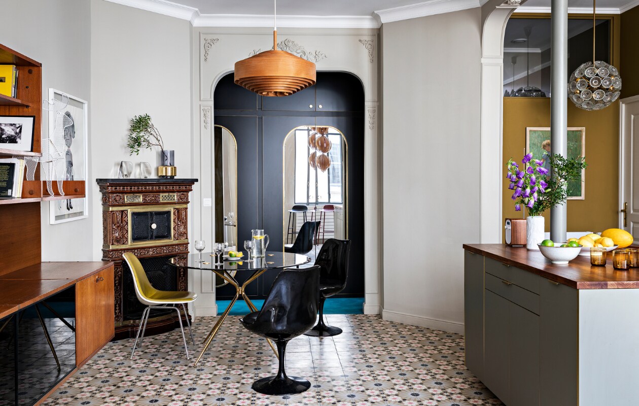 Muurverf Slipper Satin van Farrow &amp; Ball. Wandsierlijsten Orac. Vloertegels Mosaic del Sur. Teakhouten wandkast, houten hanglamp, glazen Emil Stejnar-hanglamp, eettafel en zwarte stoelen van KnollStudio vintage. , Gele stoel Eames DSX Vitra. Ingelijst kunstwerk Child van Françoise Pétrovitch. Olieverfschilderij in de keuken gevonden op de vlooienmarkt. In de op maat gemaakte wandkasten op de achtergrond zijn spiegels verwerkt. Overig onbekend.