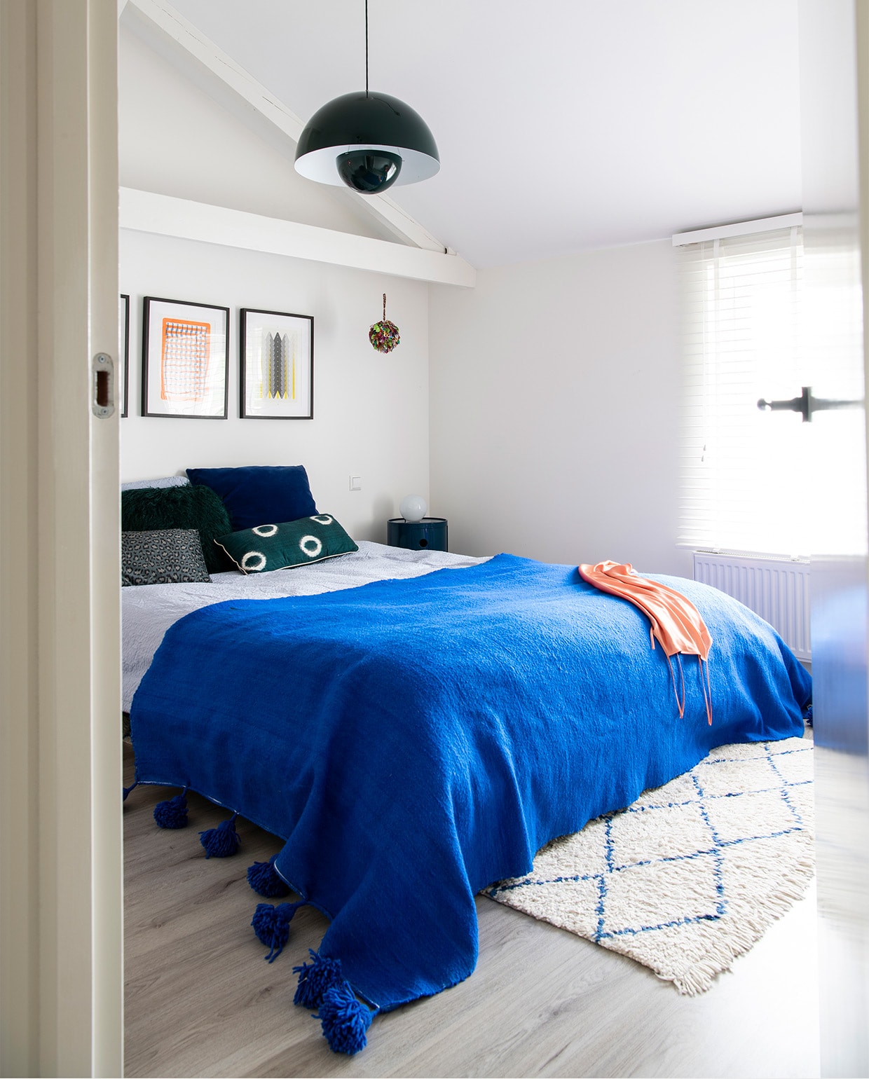 Bed Made. Blauwe sprei en vloerkleed The Souks. Hanglamp Verner Panton &amp;Tradition. Nachtkastje Kartell. Kunstwerk Risoprints Sigrid Calon. Blauw kussen Kvadrat/Raf Simons. Beddengoed Hema. Groen kussen onbekend.