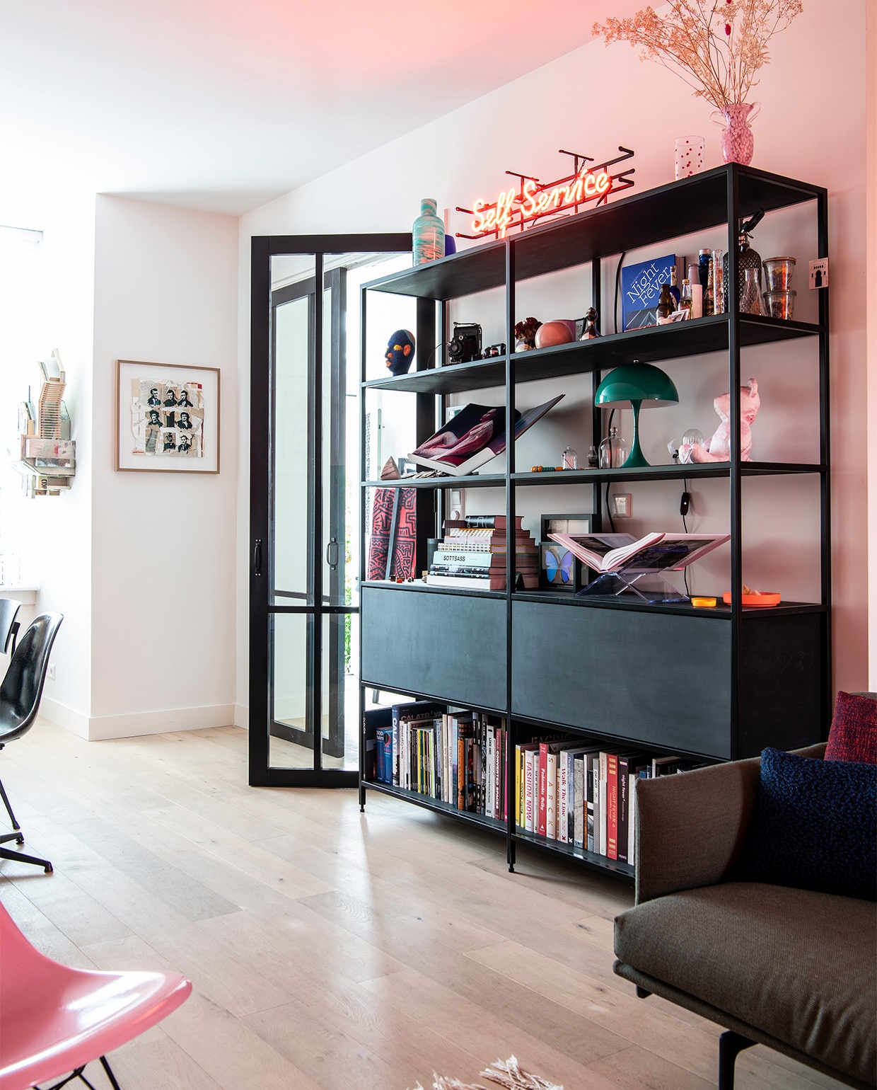 Zelfontworpen boekenkast, gebouwd door DeBeer. Neonletters uit kringloopwinkel in Zaandam. Groene vaas en vaas met roze stippen uit glasfabriek Beldi in Marrakesh. Groen lampje Panthella Mini van Verner Panton. Kunstwerken aan de muur Aldo van den Broek. Rest onbekend.