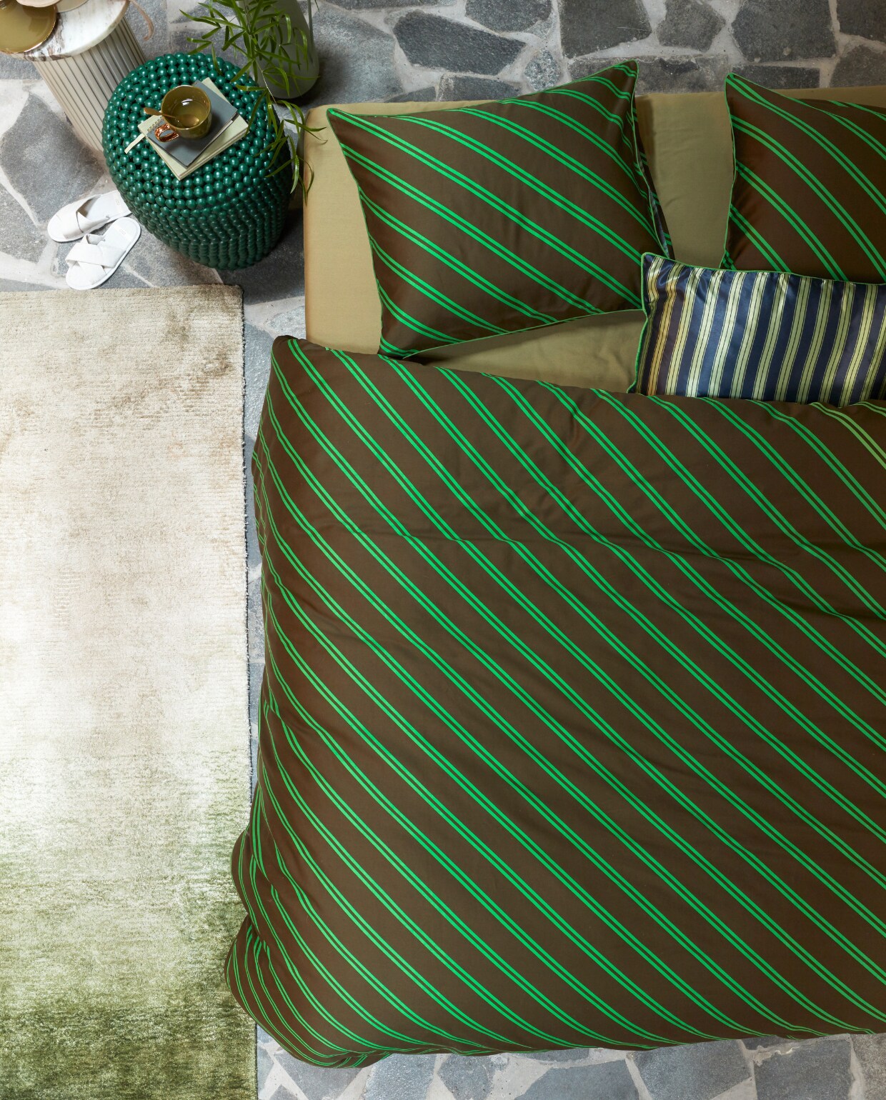 Katoensatijnen dekbedovertrek Diagonal, 140×200/220 cm € 79,95, 200×200/220 cm € 149,95, 240×200/220 cm € 159,95, 260×200/220 cm € 179,95. Satijnen kussen met bies Pyjamas, 40×60 cm € 39,95. M.m.v. made.com (vloerkleed), nordal.eu (marmeren bijzettafel Erie), polspotten.com (groene bijzettafel Dot Stool, groene metalen vaas Roman), paviljoennoord.com (mok). Overig privébezit.