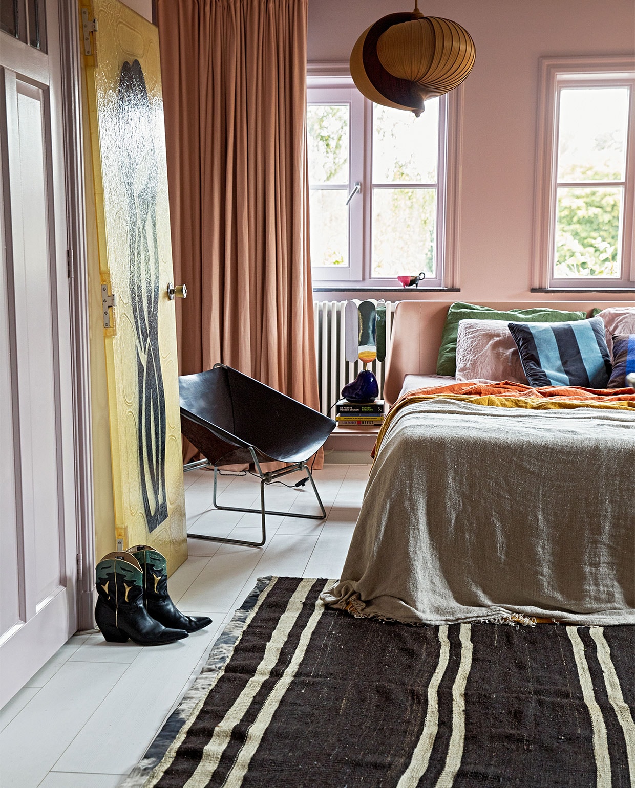 Verf wand Peach Blossom van Little Greene. Gordijnen Soft Salmon Amor Linnen van Vadain. Fauteuil Midcentury design van Pierre Paulin Polak, plafondlamp vintage Moon van Hans Agne Jakobsson, kunststuk tegen wand Fiberglass Deur Midcentrury via Best Wel Hip. Lamp nachtkastje voet van Ferm Living en kap van Hay. Bed Auping. Sprei HKliving. Kussens bedlinnen van Casa Comodo. Kleed Turks vintage. Laarzen Elena Iachi. Overig onbekend.