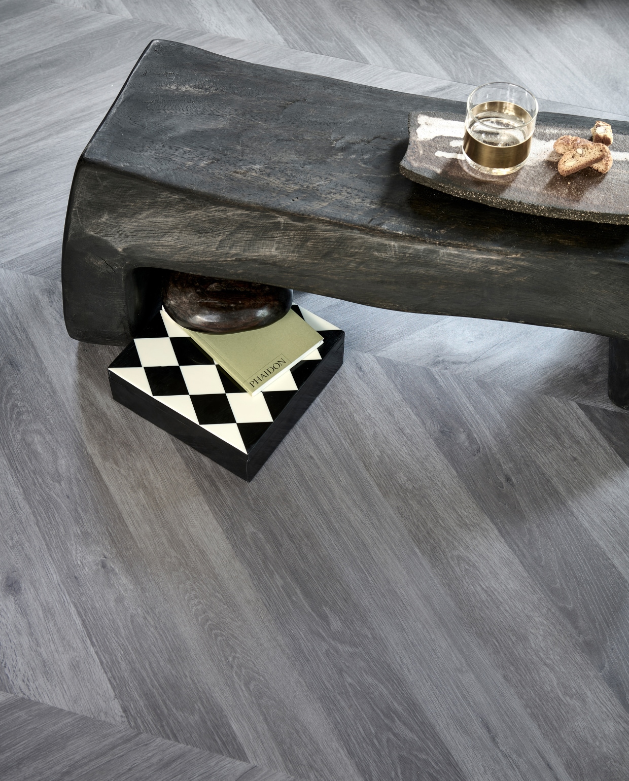 Novilon vloer Koffie, per m² € 35,65.M.m.v. interiorcowboys.com (salontafel, keramieken dienblad), vtwonen.nl (glas met messing van Serax), hm.com (doos met ruitpatroon), zarahome.com (groen boekje). Overig privébezit.