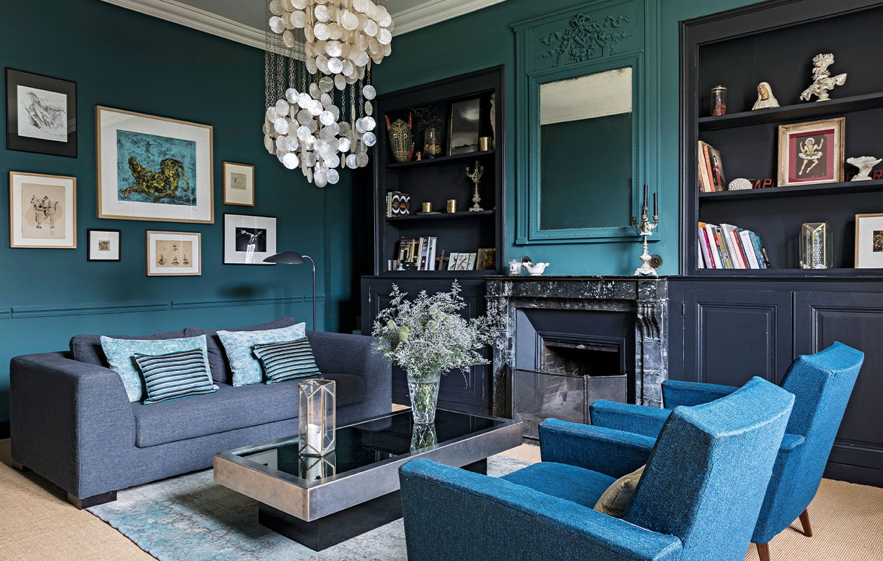 Bank van Maisons du Monde, fluwelen en zijden kussens Le Monde Sauvage, vintage salontafel van Willy Rizzo, parelmoer kroonluchter van Verner Panton, karpet gevonden in Amsterdam. Blauwe fauteuils van een rommelmarkt in Bellême. Blauwe muurverf Emery &amp; Cie, donkere muurverf Farrow &amp; Ball.