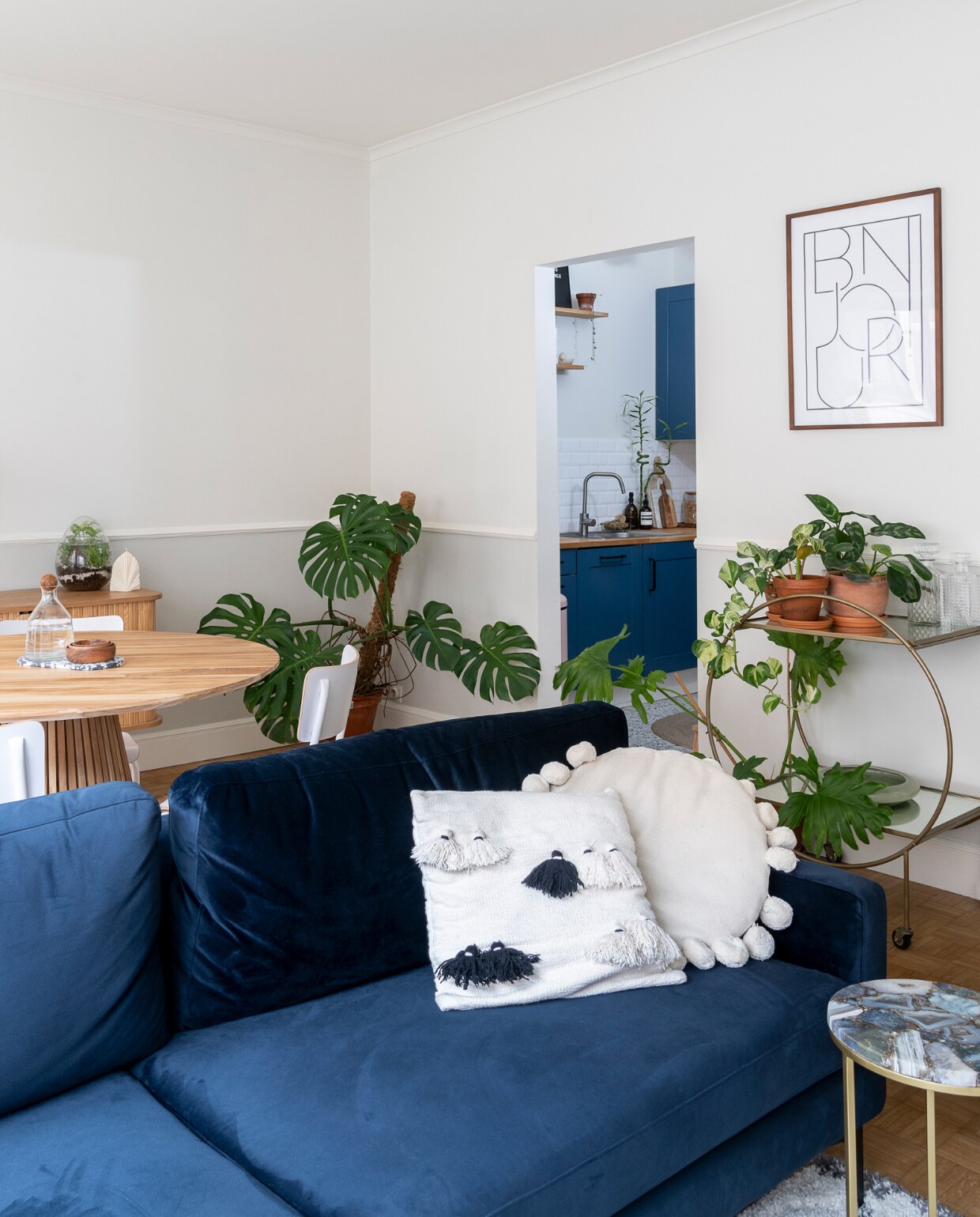 Muren geschilderd in Lovely White WE Z042 en Newspaper Grey WE Z090 van Boss Paints via Colora. Ronde tafel Fonq, blauwe bank Sofa Company, kussens La Redoute, H&amp;M Home en meegenomen uit Bali. Bijzettafel en rek op wielen Sissy-Boy. Lijst Bonjour van H&amp;M Home. Verlichting Westwing.