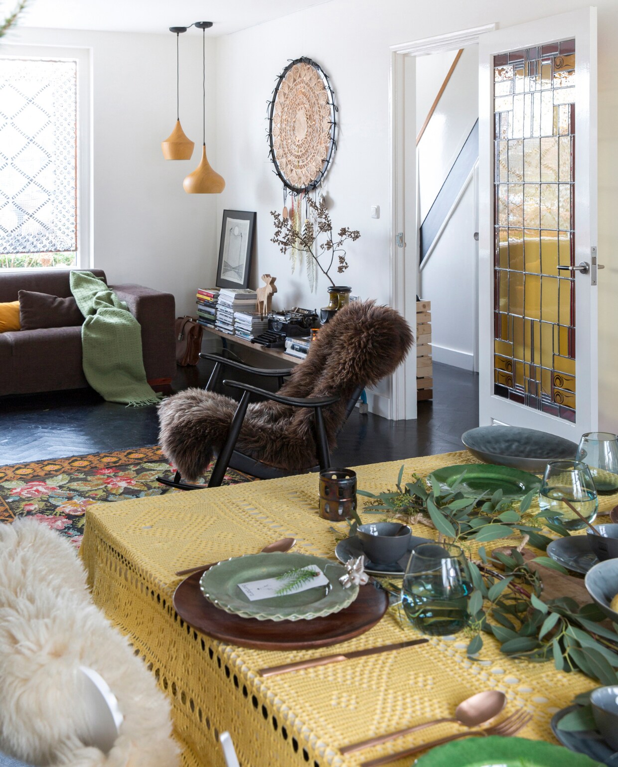 Bank Montèl, plaid Stelling Wonen, geel kussen H&amp;M Home, bruin kussen zelfgemaakt. Raambekleding zelfgemaakt. Schommelstoel grofvuil, bekleding Kay Kesting, vacht kerstmarkt De Rijp. Vloerkleed uit Moldavië. Glas-in-looddeur antiekboerderij in Krommenie. Plafondlampen Loods 5. Dromenvanger zelfgemaakt. Sidetable oude gymbank van de sportschool. Op sidetable v.l.n.r. schilderij uit Portugal, tijdschriften, houten hert Stelling Wonen, vintage typemachine, boeken, vaas Berlijnse rommelmarkt. Servies, glaswerk, bestek, kaars met ster, groene keramieken kan K’ook!. Vlinderstoel Fritz Hansen, witte vacht Ikea. Groene takken Floribundus. Visgraatvloer Van Dijk &amp; Ko, zwart geschilderd en gelakt met producten van Sigma, muurverf RAL 9010 en matzwarte muurverf.