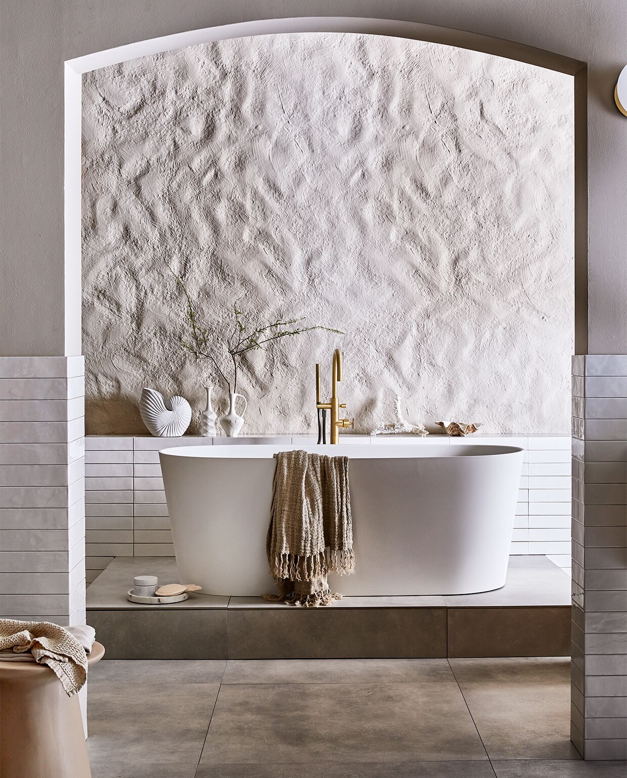 Vloertegel Mold XL Cement, 90×90 cm. Wandtegel achter wastafel Marrakesh, kleur Nieve, glans, 6,5×40 cm (lxb). Wastafel Tank, beton, kleur Concrete, 10x120x46 cm (hxbxd). Onderbouwkast Cube, eikenhoutfineer, kleur Oak, 30x120x43,5 cm (hxbxd). Wandkraan Flame, kleur Bronze, inbouwdeel. Bad Tub. Badmengkraan Flame, kleur Bronze, vrijstaand M.m.v. vtwonen.nl (muurverf kleur Flax, spiegel Ferm Living, wafelhanddoek Marc O’Polo), hkliving.nl (kruk, kleine witte vazen), nordal.eu (grote schelp, schelpvormige vaas, linnen badlakens, marmeren zeepdispenser), weldaad.com (marmeren schaaltje), hm.com (loper, grote marmeren schaal op vloer). De achterwand kreeg stuc effectief in kleur Flax van vtwonen (gemaakt door setbouw Milo Kol).