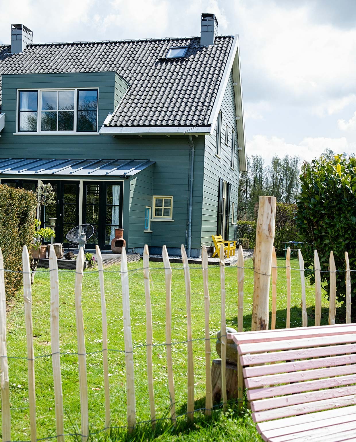 Het huis is aan de buitenkant afgetimmerd met hout, maar heeft een betonnen constructie. De kleur is bepaald door de monumentencommissie en mag niet worden veranderd. Tuinbank van de kringloop geschilderd in Nancy’s Blushes van Farrow &amp; Ball.