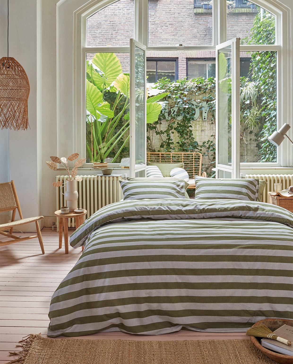 Katoenen dekbedovertrek van vtwonen collectie Bold Stripe, kleur Green,140×200/220 cm € 59,95, 200×200/220 cm € 109,95, 240×200/220 cm € 119,95, 260×200/220 cm € 139,95 (ook verkrijgbaar in Peach). Op de buitenbank gestreept kussen Bold Round, gerecycled acryl en polyester, kleur Green, 40 cm (Ø) € 49,95, gestreept kussen Bold Square, gerecycled acryl en polyester, kleur Green, 45×45 cm € 44,95. M.m.v. sissy-boy.eu (fauteuil, rotan takken), nordal.eu (hanglamp, nachtkastje), loods5.nl/goods (houten bijzettafel), letoile.store (mok, wierookhouder, vloerkleed), mimiettoi.com (houten schaal, tafellamp). Overig privébezit.