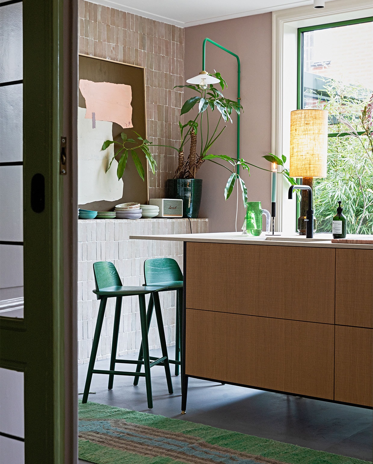 Groene lamp aan muur Valerie Objects. Tegels Bejmat Gris rose Marokkaanse tegels via Design Tegels. Schemerlamp en kunst HKliving. Kandelaar Hema. Kan Hay. Plantenpot Serax. Muziekbox Marshall. Servies mix van onder andere Home Chef en 70’s ceramics van HKliving. Krukken Nerd van Muuto. Keuken Unit van Cesar Kitchens. Kleed vintage berber. Aluminium pui in kleur Varen Groen. Lamp plafond onbekend.