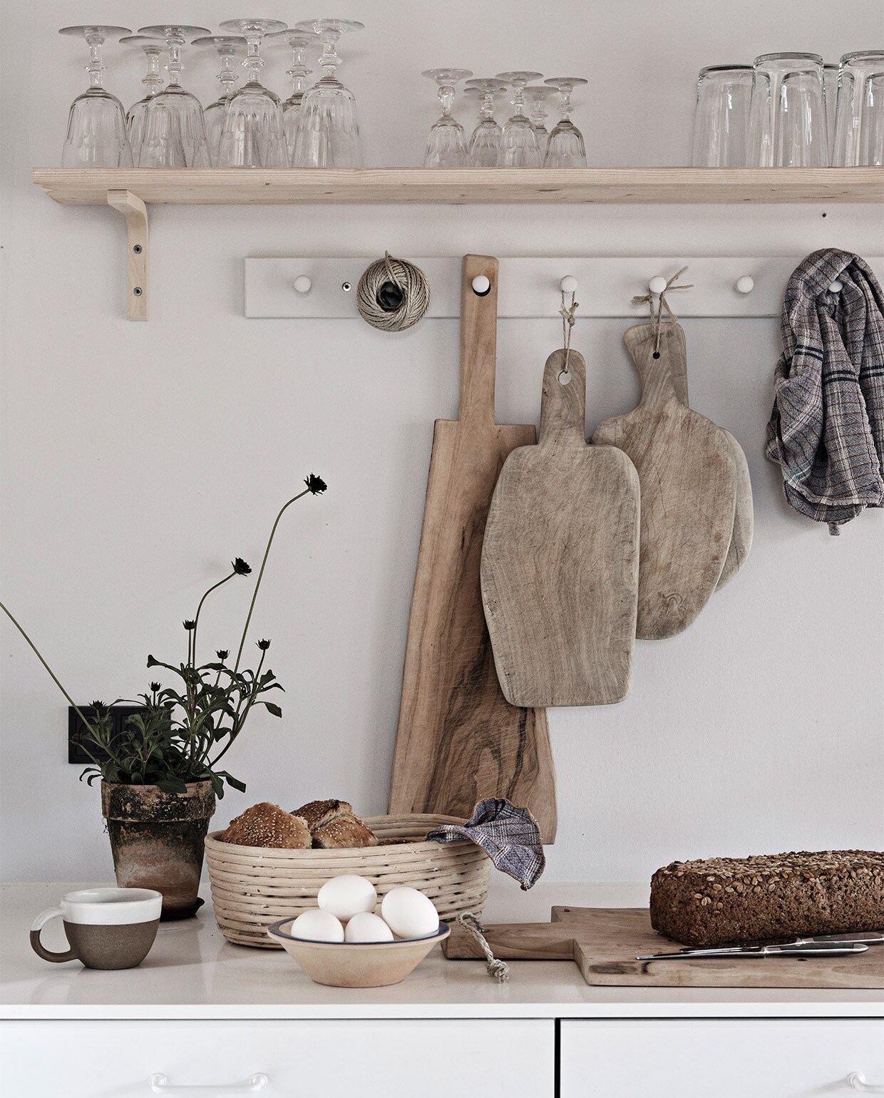 Keuken, wandrekken, glazen en hoge krijtwitte vaas Ikea. Eettafel en snijplanken Andrea Brugi. Metalen stoel Egon Eiermann, houten stoelen vintage. Vergelijkbare plafondlamp Lampion. Wandlampen Serge Mouille. Theeketel Le Creuset. Zilveren kan uit Griekenland, groen bord uit Marokko. Theedoek Aiayu. Overig onbekend.