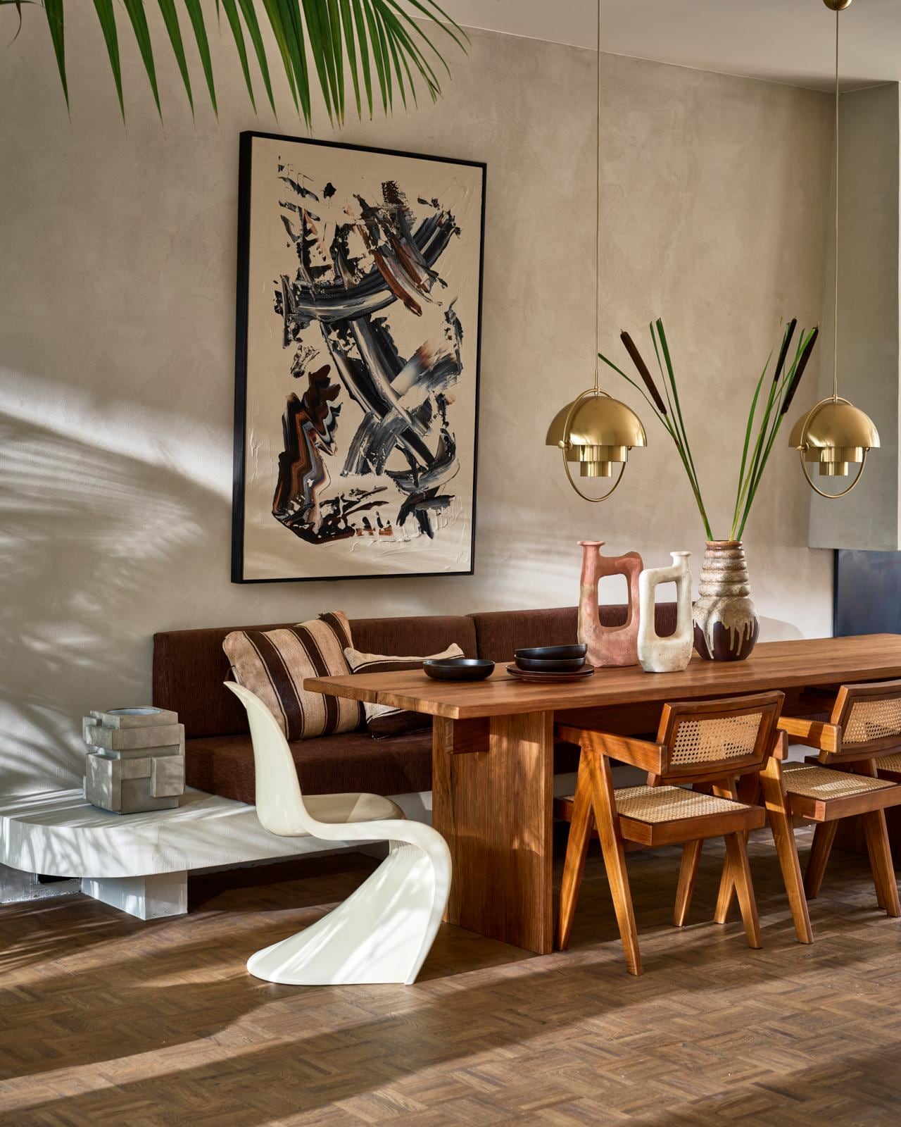 Op maat gemaakte tafel van frakéhout, prijs op aanvraag (@takumi_interior). Abstract schilderij van Patrick van Riemsdijk (patrickvanriemsdijk.com). Tamegroute vaas, klein € 115,-, groot € 138,- (householdhardware.nl). Houten armstoelen Detjer Office Chair, € 425,- (casagitane.com). Hanglampen Multi Lite Pendant Large Brass van Gubi, € 839,- (nordicnew.nl). Vintage jaren 70- vaas € 50,- (vandijkenko.nl). Witte kunststof stoel Panton Chair van Verner Panton uit 1974, € 750,- (neeflouis.nl). Donkerbruine keramische borden Home Chef, diep € 16,95, plat € 17,95 (hkliving.nl). Betonnen wijnkoeler € 149,- (serax.com). Bruin/beige gestreept kussen, 50×60 cm € 149,-, bruin/beige gestreept kussen, 60×40 cm € 149,- (couleurlocale.eu).