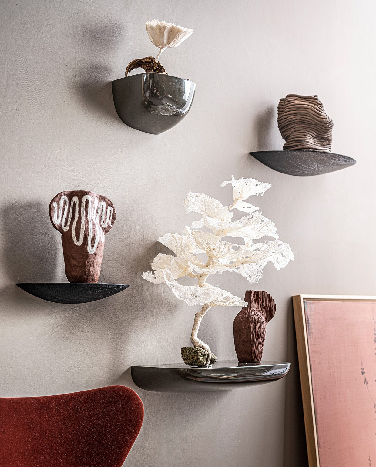 Op wand krijtverf in kleur Drift, per liter € 39,25 (pure-original.nl). Grijze wandplanken van Vitra, per stuk vanaf € 58,-, zwarthouten wandplanken van Menu, per stuk vanaf € 65,- (vtwonen.nl). Terra kunstobjecten van Maria Lenskjold, prijs op aanvraag (theodeto.com). Kunstobjecten van papier op houten en stenen sokkel, prijs op aanvraag (elsavisser.com). Bruine vaas Wobbly Vase € 240,- (2222studio.com). Roodfluwelen stoel € 649,- (kasstoor.nl). Schilderij van Maartje van den Noort, prijs op aanvraag (maartjevanden­noort.nl).