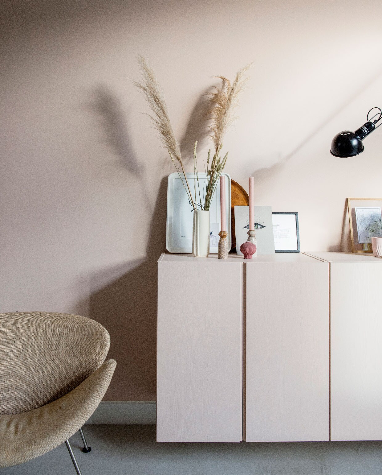 Muurverf Setting Plaster van Farrow &amp; Ball, vloer Leef-Beton gelegd door Het Nieuwe Stenen Tijdperk. Vintage stoel Orange Slice van Artifort Marktplaats. Ikea kastjes geschilderd in de kleur van de muur. Witte fotolijst Ikea, witte vaas en kaarsenhouders kringloop, kaarsen Winand Hazelaar. Print oog gemaakt door dochter Julia, zwarte fotolijst Desenio, houten fotolijst Moebe met daarin in een plattegrond van Zwolle. Wandlamp 265 Flos.