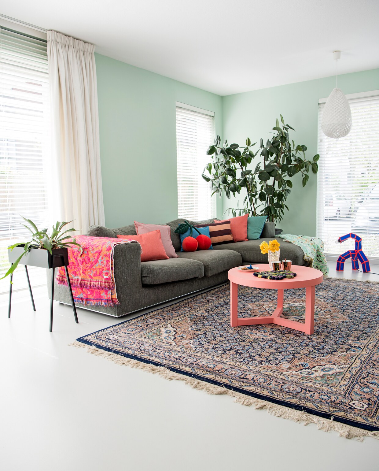Bank Goossens. Gekleurde kussens Roos Soetekouw, kersenkussen merimeri.com, gestreept kussen HK Living. Roze Fringe plaid no. 1 en 5, Fun green Roos Soetekouw. Kleed marktplaats.nl. Plantenbak Kwantum. Witte lamp Studio Arntzen. Paper &amp; Tape lamp annebetphilips.com. Salontafel Zilverblauw voor Wown. Kopjes Pols Potten. Vaasje kringloop. Muurverf kleur Karma van Histor.