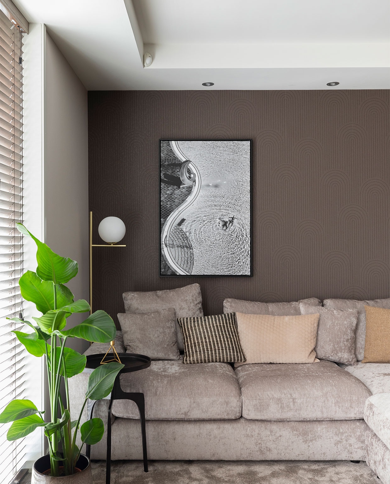 Flexa Creations muurverf Sandy Steps (flexa.nl). Bamboe jaloezieën kleur 1523, prijs op aanvraag, vloertapijt Ambiant Boston Mokka 0610, prijs op aanvraag (woninginrichting-aanhuis.nl). Kunstwerk Zwembad van Jure Kravanja, in deze uitvoering € 261,- (werkaandemuur.nl). Behang Artifact 312436, prijs op aanvraag, gordijnen Patience 7137-3, prijs op aanvraag (eijffinger.com). Gordijnen op maat gemaakt, prijs op aanvraag (gordijnprodukties.nl). Vloerlamp Pure van Trio € 124,99, (vtwonen.nl). Bijzettafel Pano van Lightmakers, maat S € 79,99, maat M € 179,-, hoekbank Couchbuddy van Eijerkamp Collectie € 4584,-, kussens vanaf € 6,99, ronde poef Claudi € 249,-, Op bijzettafel kandelaar Triangle van Housevitamin (housevitamin.nl). Plant naast bank Strelitzia € 79,50, pot € 59,50. Overig privébezit.
