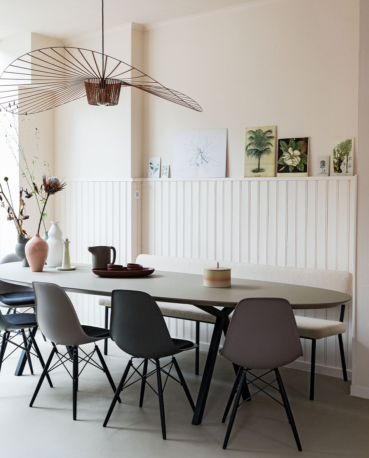 Tafel en bank Studio Henk. Lamp Petite Friture via Eijerkamp. Stoelen Eames via Vitra. Koektrommel HKliving. Witte vaas Household Hardware. Roze vaas De Bijenkorf. Grijze vaas vtwonen. Lichtgrijze vaas en waterkan Ikea. Kandelaar herkomst onbekend. Botanische platen zelfgemaakt. Wanden, lambrisering en plafond kleur Julie’s Dream van Little Greene. Vloer Lab Cementum kleur Brown Wood van Vestingh Paint. Stopcontact De Oude Schakelaar.