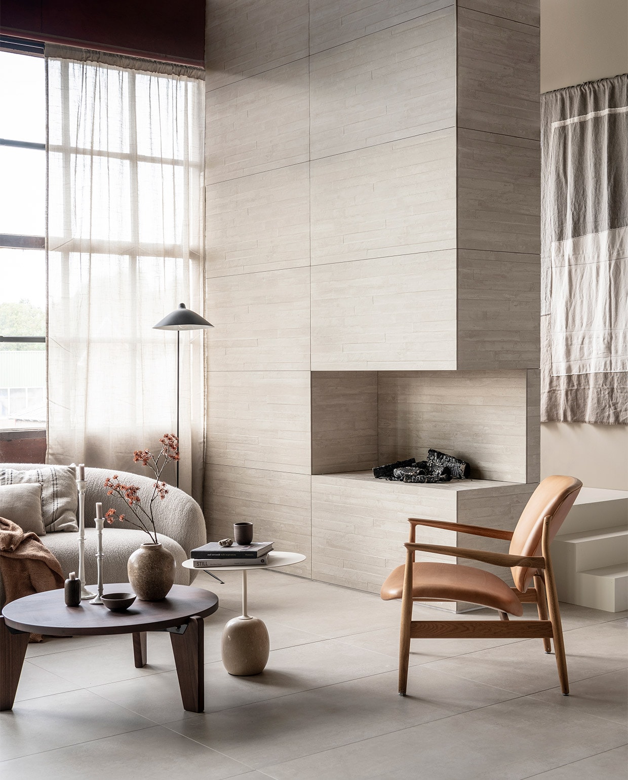 Op de wand: wandtegel Raw Casa Decor 3D in kleur Sand, 60×120 cm,-. Op de vloer: vloertegel Raw in kleur Sand, 0×120 cm. | M.m.v. justhaasnoot.nl (staande lamp, bank Julep van Tacchini, salontafel Guéridon Bas van van Vitra, witte bijzettafel Lato van &amp;Tradition, fauteuil van hout met leer van House of Finn), zarahome.com (witte metalen kandelaars, stenen vaas), suhka.nl (textielkunstwerk, kom en mok). Overig privébezit.