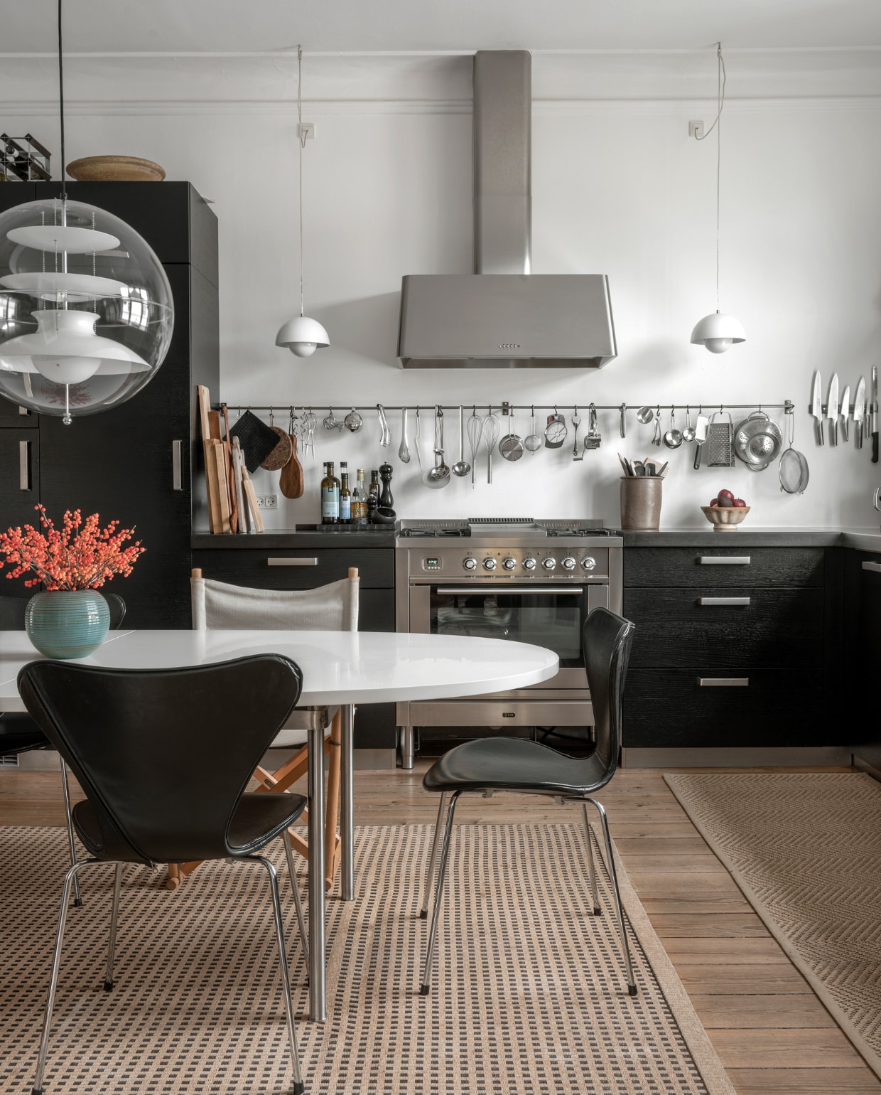 Tafel Marianne Wegner, twee Series 7 stoelen van Arne Jacobsen, vouwstoel Mogens Koch, hanglamp Globe boven de tafel en witte hanglampen Flowerpot boven aanrecht, alles Verner Panton. Fornuis en afzuigkap Ilve, ruim twintig jaar oud papiergaren vloerkleed van Woodnotes, stalen planken Ikea. Overig onbekend.