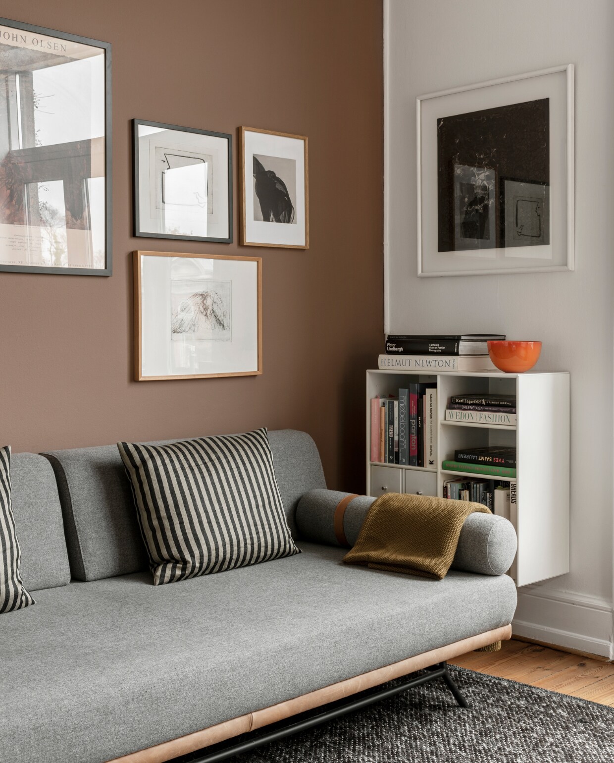 Daybed REM van Sofacompany, boekenkast Montana, erboven een ingelijste tekening op zijde, cadeau gekregen. Kunst aan de muur, met de klok mee: poster van kunstwerk John Olsen, tekening van Ida Mortensen, poster maker onbekend, tekening van Birgitte Krog. Overig onbekend.