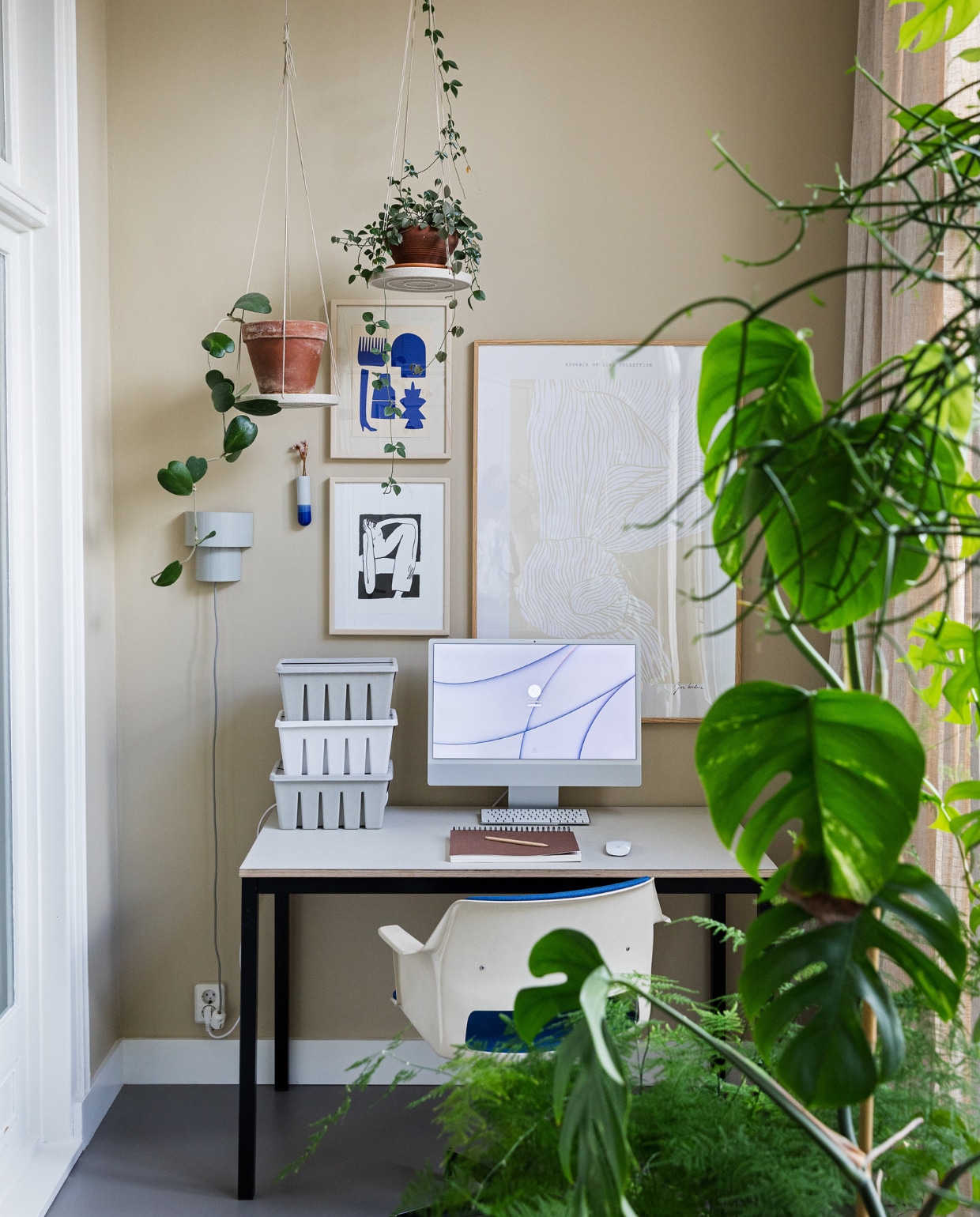 Muurkleur GN 080-08. Bureau zelfgemaakt van oud frame en linoneum blad. Bureaustoel Gispen. Print blauw van Silvia Visscher, print zwart-wit van Lucia Lenders, print beige, opbergdozen, wandvaasje van Harm en Elke, planten via Nørd Conceptstore. Wandlamp rommelmarkt. Plantenhangers Bloomingville.