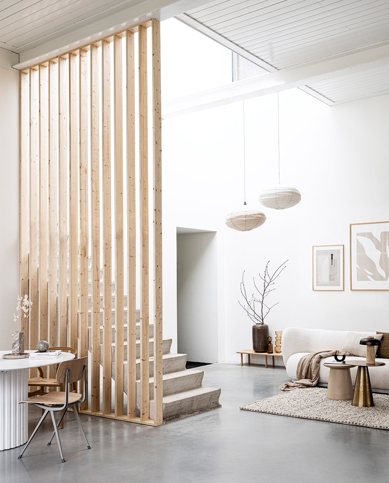 Scheidingswand gemaakt van latten uit vtwonen DIY 09-2020. Laag houten wandmeubel Loof Piled, 24x150x35 cm (hxbxd) € 275,-, zwarte kandelaar Arch van Ferm Living € 45,99 (vtwonen.be). Marmeren bol € 29,99, bouclé plaid 130×170 cm € 14,99 (hm.com). Grote vaas Jade achter trap € 99,95, bruine glazen vazen achter trap vanaf € 32,95, linnen kussens 40×40 cm € 39,95 en 40×60 cm € 45,- (loods5). Wollen vloerkleed Hjorthede, 160×230 cm € 299,- (ikea). Messing bijzettafel 49×49 cm (Øxh) € 239,-, aardewerken bijzettafel 40×43 cm (Øxh) € 195,- (hkliving). Bouclé 3-zitsbank Rico van Ferm Living, 210x79x81,5 cm (bxhxd) € 3389,- (flinders). Posters: groot Fragments van Moe Made It, 70×100 cm met eikenhouten lijst € 109,- klein Carrarra van Julia Hallström Hjort, 50×70 cm € 89,- met eikenhouten lijst € 69,- (theposterclub.com). Boeken privébezit.