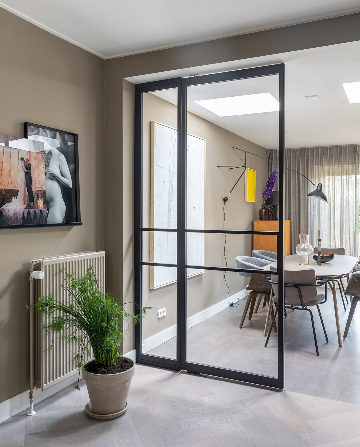 Aluminium tussenwand met deuren prijs op aanvraag (gewoongers). Flexa Creations muurverf in de eetkamer Brave Ground, in de keuken Worthy Clay (flexa). Massief eikenhouten visgraatvloer, licht gerookt en afgewerkt met olie prijs op aanvraag, betonlook pvc vloer prijs op aanvraag (woninginrichting- aanhuis). Transparante gordijnen Jetze prijs op aanvraag (eijffinger.com). Aluminium deuren prijs op aanvraag (gewoongers). Oven, kookplaat prijs op aanvraag (atag.nl). Tafel Tree van Woud € 1199,-, grijze stoelen Catch van BePureHome, per stuk € 159,-, bruine stoelen Patch van Bodilson, per stuk € 239,-, zwarte wandlamp Mantis € 950,- (eijerkamp). Groot wit kunstwerk naast tafel Brutalism € 595,-, felgeel kunstwerk € 195,- (hkliving.nl). Hanglamp Marlon € 78,99 (zuiver.com). Tafellamp op de wandplank in de keuken Athens € 73,- (itsaboutromi). Vaas van HKliving € 39,95, zwarte kandelaars per stuk vanaf € 15,25 (vtwonen.be). Overig privébezit.