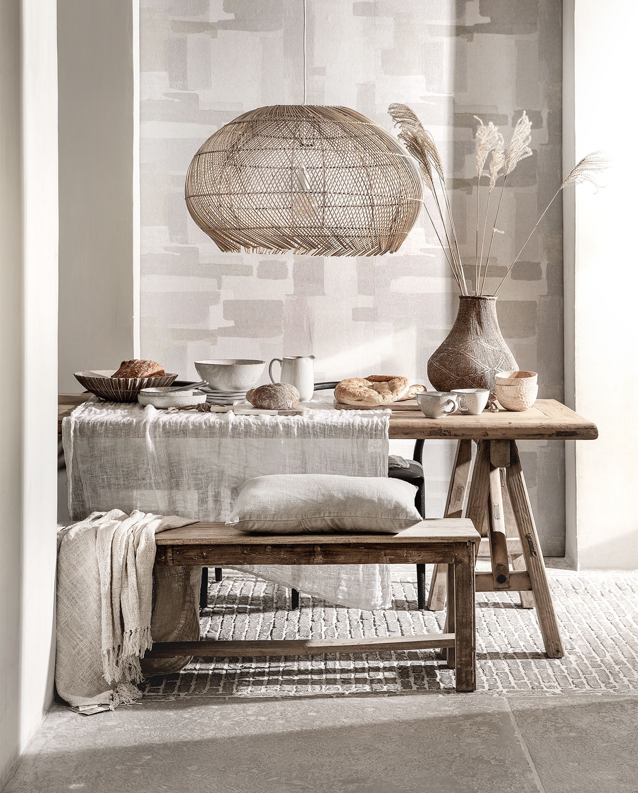 Behang Lino, 106 cm breed per meter € 15,95 (eijffinger.com). Rieten hanglamp € 229,95 (manggisliving.nl). Houten whitewash schaal Marseille € 92,50 (mrsbloom). Servies Broste Copenhagen; schalen v.a. € 19,95, grote schaal € 39,95, kan € 33,95, bord € 11,95, grote kom met oor € 15,95, bewerkte houten schaaltjes per stuk € 39,95 (loftloft). Linnen kussen € 49,95, eettafel van oud hout, 260×90 cm € 1795,-, oud teakhouten bank 176 cm breed € 245,- (hetkabinet). Grof geweven plaid € 87,95 (heinshome.nl). Vaas € 69,- (stylexclusief.nl).
