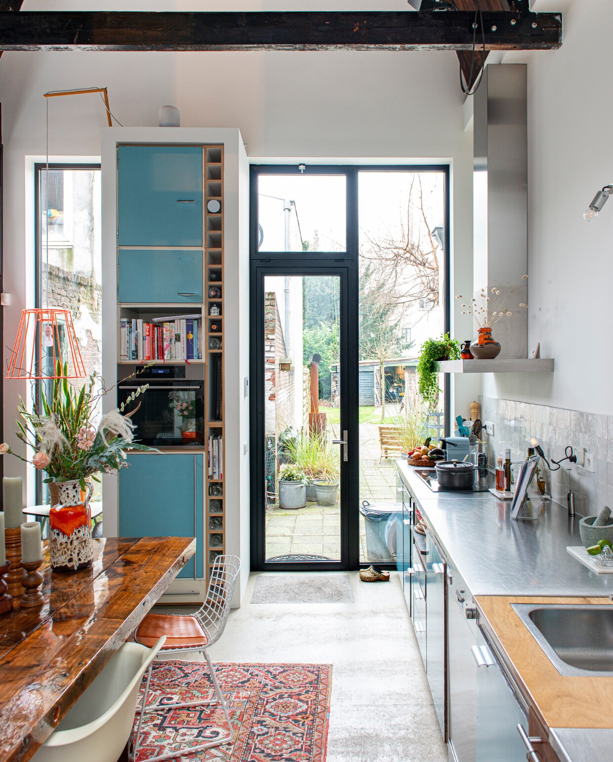 Keuken van Piet Zwart voor Bruynzeel, tafel zelfgemaakt, witte stoel Eames Plastic Armchair voor Vitra, ijzerdraad stoel Wire Chair van Harry Bertoia voor Knoll, spot Nomad van Modular, Perzisch tapijt vintage, hanglamp zelfgemaakt van een oude lampenkap en oranje garen, oven Ikea, houten kandelaars kringloopwinkel, keramieken vaas van de Noordermarkt in Amsterdam. Overig onbekend.