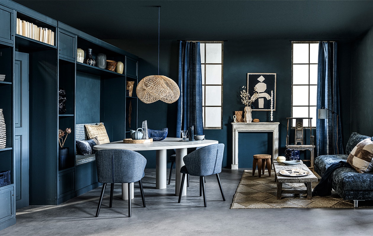 Op de wand krijtverf Steel Blue, per liter € 39,25 (pure-original.nl). Kastenwand en eettafel, prijs op aanvraag (com-anders.nl). Zit- en rugkussen bekleed met stof Rolf uit de Fashion Weaves 3-collectie van Nobilis, per meter € 135,-, gordijnen gemaakt van stof Pasadena Sheer Vintage Indigo van Ralph Lauren, per meter € 206,-, fluwelen kussen met kleurvlakken Aritha Slates van William Yeoward € 117,-, vloerlamp Farnham van Vaughan € 1087,- (wva.nl). Zwart-naturel gevlochten mand € 69,-, houten dienblad € 79,- (sukha.nl). Krat € 12,-, draadmand € 74,85 (loods5.nl/design). Blauwe organisch gevormde vazen Tuck van Ferm Living, groot € 148,99 en klein € 65,99, waterglas van Serax, per 4 € 43,99, blauwe karaf Terres de Rêves van Serax € 54,95, grijze kom Rur:al van Serax, Ø18 cm € 30,-, jeansblauw XL bord van Serax, Ø 36 cm € 99,- (vtwonen.nl). Beige vaas met lichte onderkant € 39,95, grijze glazen vaas met streepstructuur € 99,95, houten vaas € 22,90 (loods5.nl). Blauwe glazen vaas met streepstructuur € 115,-, blauwe keramieken vaas met witte strepen € 49,50, object op voet met witte schelpen € 109,- (covanderhorst.nl). Beige vaas € 19,99, offwhite organisch gevormde vaas € 39,99, beige keramieken opberger met deksel € 12,99, vergrijsd blauw bord € 7,99 (hm.com). Gevlochten kussen € 119,-, rotan hanglamp € 195,-, juten vloerkleed € 1199,-, houten kruk € 335,-, salontafel € 1650,-, raffia schaal € 89,-, oude Chinese tempelstoel € 1390,-, plaid Indigo Bogolan, 95×140 cm € 125,- (couleurlocale.eu). Langwerpig donker houten object in kast € 219,90 (badenbaden.nl). Licht houten object in kast privébezit. Eetkamerstoel Waldo, 59×52,5×80 cm (bxdxh) € 179,- (dutchbone.com). Blauwe keramieken kan met handvat € 80,- (paviljoennoord.com). Glazen karaf € 35,- (fermliving.com). Antieke schouw € 650,- (oudebouwmaterialen.nl). Kunstwerk uit The Heritage Series, prijs op aanvraag (irisdorine.com). Witte keramieken lus € 30,-, staand houten object op schouw € 130,-, liggend houten object op schouw € 48,- (studio-yen.com). Blauwe fluwelen bank, 230x80x97 cm (lxbxd) vanaf € 2686,- (kasstoor.nl).