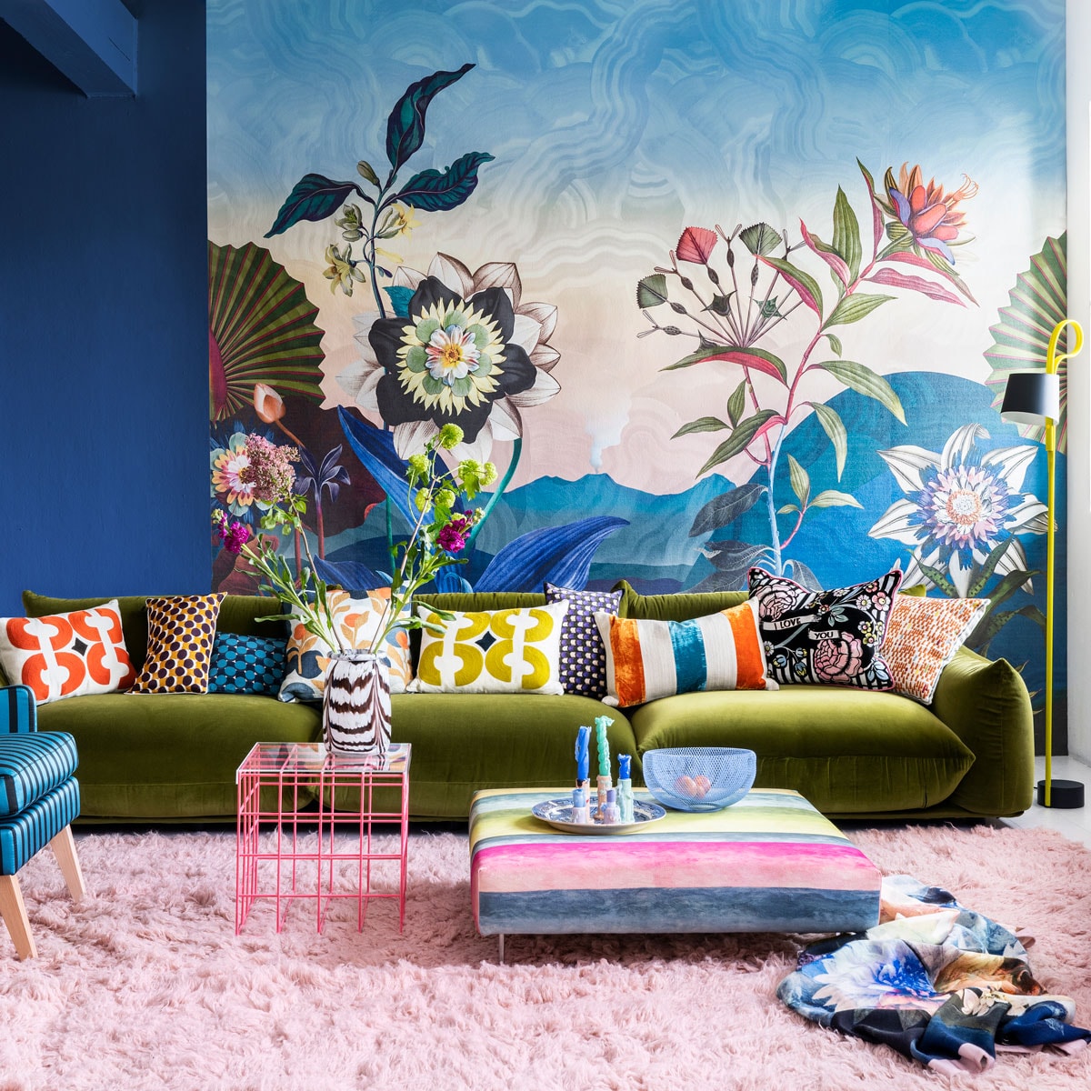 Paneel met behang Atlantis Aube van Christian Lacroix voor Designers Guild, 300×350 cm € 927,- (wva.nl). Blauwe muurverf Exciting Night No. 96 van Lab Paint, per liter € 45,- (vestingh.nl). Groene velours bank van Arflex, 96x354x70 cm (dxbxh) € 5709,-, roze fauteuil van Warm Nordic, 95x84x80 cm (lxbxh) € 2190,-, zachtroze hoogpolig wollen vloerkleed van Layered, 250×350 cm € 1090,- (goeds.nl). Multikleurige voetstoel in stof Rayure Chinoise Alchemilla van Designers Guild, 90×90 cm € 1485,-, oorfauteuil Harper Chair bekleed met stoffen van Christian Lacroix voor Designers Guild € 3220,- (wva.nl). Verstelbare vloerlamp € 659,- (hay.nl). Roze staaldraad tafel van Bold Monkey, 41x41x40 cm (lxbxh) € 165,- (boldmonkey.com). Kandelaars vanaf € 14,50, kaarsen van Hay, per 6 € 25,- (vtwonen.nl). Glazen vaas € 85,- (hay.nl). Vintage bord € 25,- (hetgroteavontuur.nl). Blauwe gaasschaal € 39,- (festamsterdam.com). Kussens van links naar rechts: rood geborduurd € 149,-, langwerpig model van zijde, per stuk € 89,- met bloemdessin € 109,-, groen geborduurd € 149,-, alles van Lelievre (loggerewilpower.com), velours streep van William Yeoward € 121,-, bloemen Christian Lacroix voor Designers Guild € 192,-, geborduurd € 132,-, wollen plaid van Designers Guild € 327,- (wva.nl).