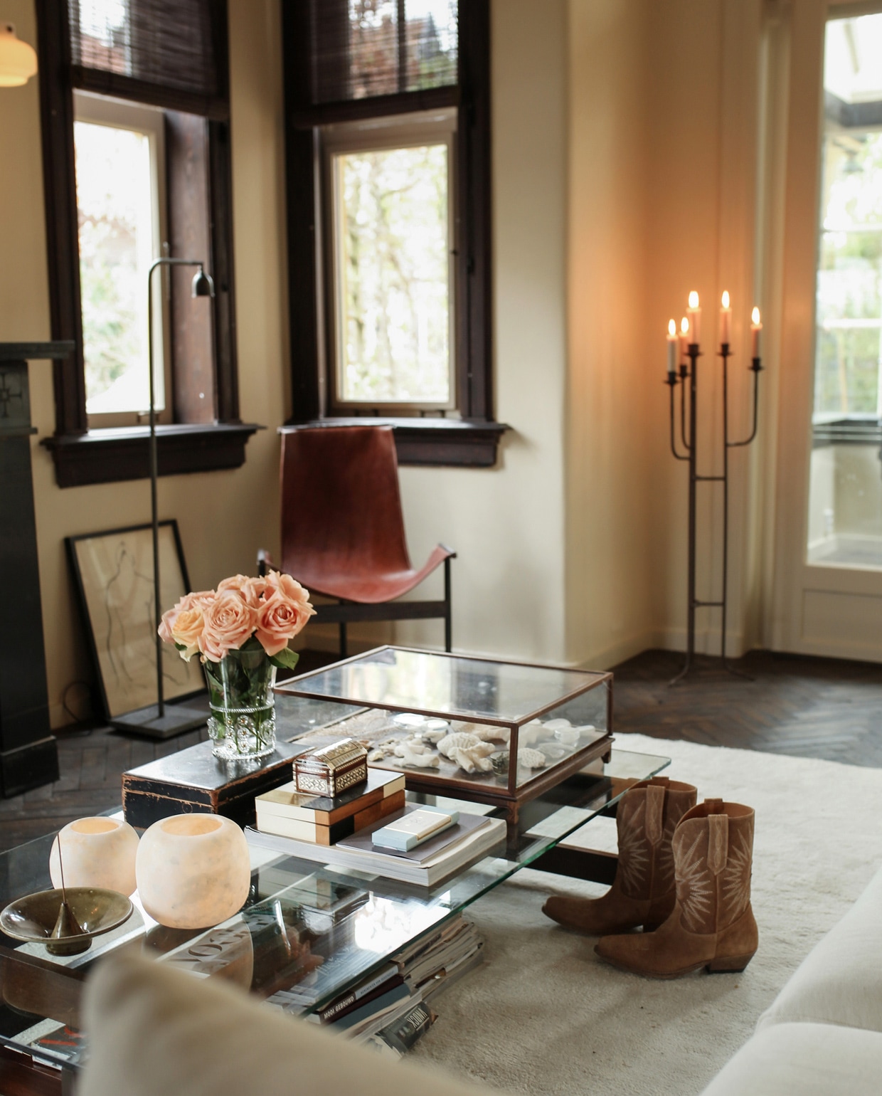 Leren fauteuil en vloerlamp Brecht Murré Atelier. Salontafel met vitrinekast vol natuurvondsten in het buitenland gekocht. Bank l’Authentique, op maat gemaakt vloerkleed Cunera, kaarsenkandelaar tweedehands. Stolp Pols Potten. Overige op tafel kringloopwinkel.