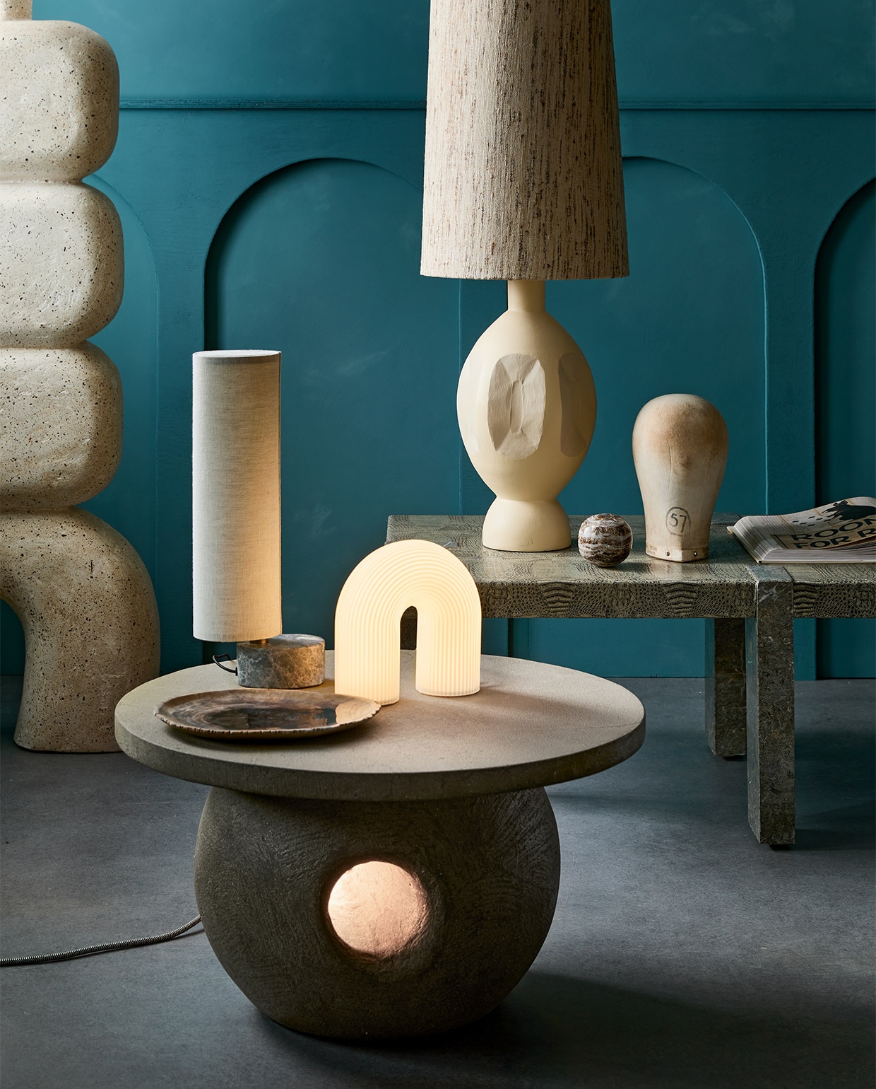 Kalkverf op de muur 87 Petrol, 2,5 liter € 126,-(lauthentique.nl). Tafel met licht € 800,-, links: voet van sculpturale vloerlamp van microcement € 1150,-(lanena-home.com). Witte tafellamp Vuelta van Ferm Living € 199,- (vtwonen.nl). Tafellamp met marmeren voet Unbound van Gubi vanaf € 549,- (gubi.com). Keramieken lampvoet Boho € 179,-, kap € 109,95 (hkliving.nl). Object hoofd, prijs op aanvraag (vandijkenko.nl). Overig privébezit.