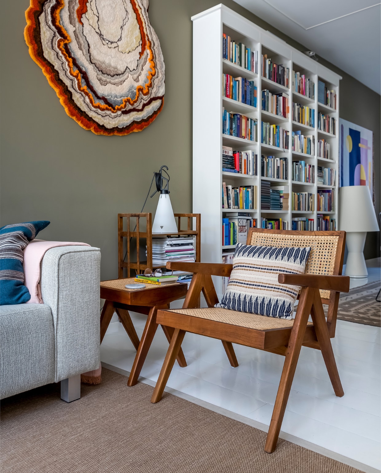 Muurverf Tent van Flexa, wandkleed links Lizan Freijsen, boekenkast Lundia, wandkleed rechts Kukka. Bank Hulshoff, kussens HKliving, deken Hay, lamp links Floss, houten boekentafel onbekend, webbing stoel en bijzettafel Detjer. Lamp rechts de Bijenkorf, merk onbekend. Herkomst Afghaans vloerkleed onbekend, vloer witte epoxylak over oud parket.