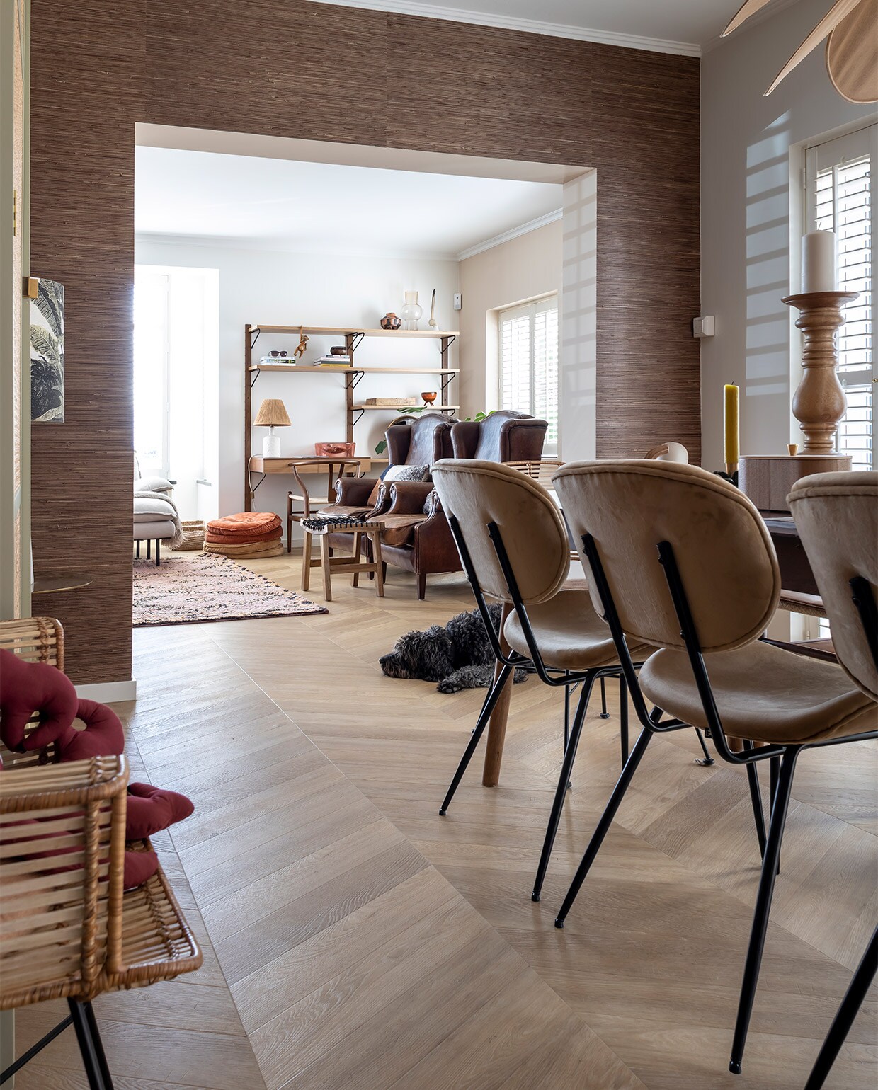 Muurkleur Flexa Gentle Umber. Behang Eijffinger Natural grasweefsel. Vloer Hongaarse punt pvc Therdex 6541. Houten stoelen Wishbone Chair, uitschuifbare tafel Sohome, gele kaars Sissy-Boy, kaarsenstandaard Loft Arnhem, rotan stoelen en drie stoelen rechts, rond kussen, kleed en plantentafel HKliving. Kast en spiegel Ikea Stockholm-lijn, vaasjes Zara home, lamp Archive Store. Shutters Veneta.