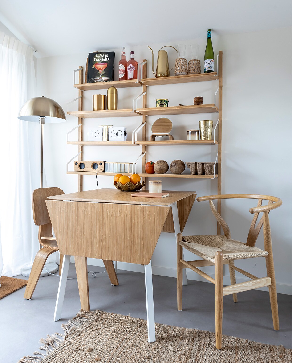 Vloerlamp It’s About Romi, uitklaptafel Ikea, stoel links Eames DCW Replica, stoel rechts Wishbone Chair, vloerkleed, waterkaraffen, spiegel en geurkaarsen in pot HKliving. Gieter Sissy-Boy, ijsbak Bloomingville, cocktailshaker Bloomingville, theedoosje Xenos, flipclock Karlsson, soundbox House of Marley, glazen doos Kwantum, fruitschaal Zara Home, boek Yaya. Plankensysteem Ikea.