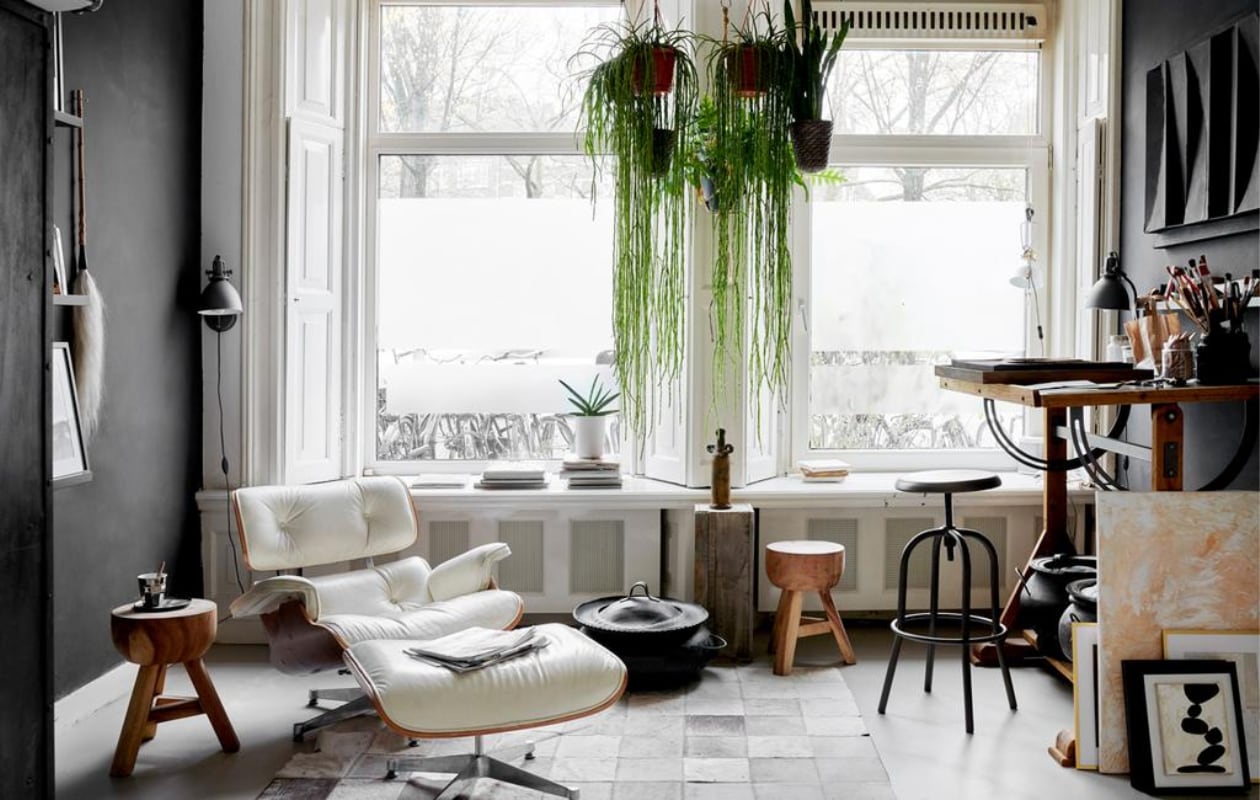 Het atelier in de voorkamer met lounge chair en ottoman van Eames voor Vitra. Tekentafel, krukken en slagersrek Marktplaats. Lamp Serge Mouille. Leren karpet overgenomen van een vriend. Mand uit Marokko. Sokkel van een markt, de vaas erop is een reissouvenir.