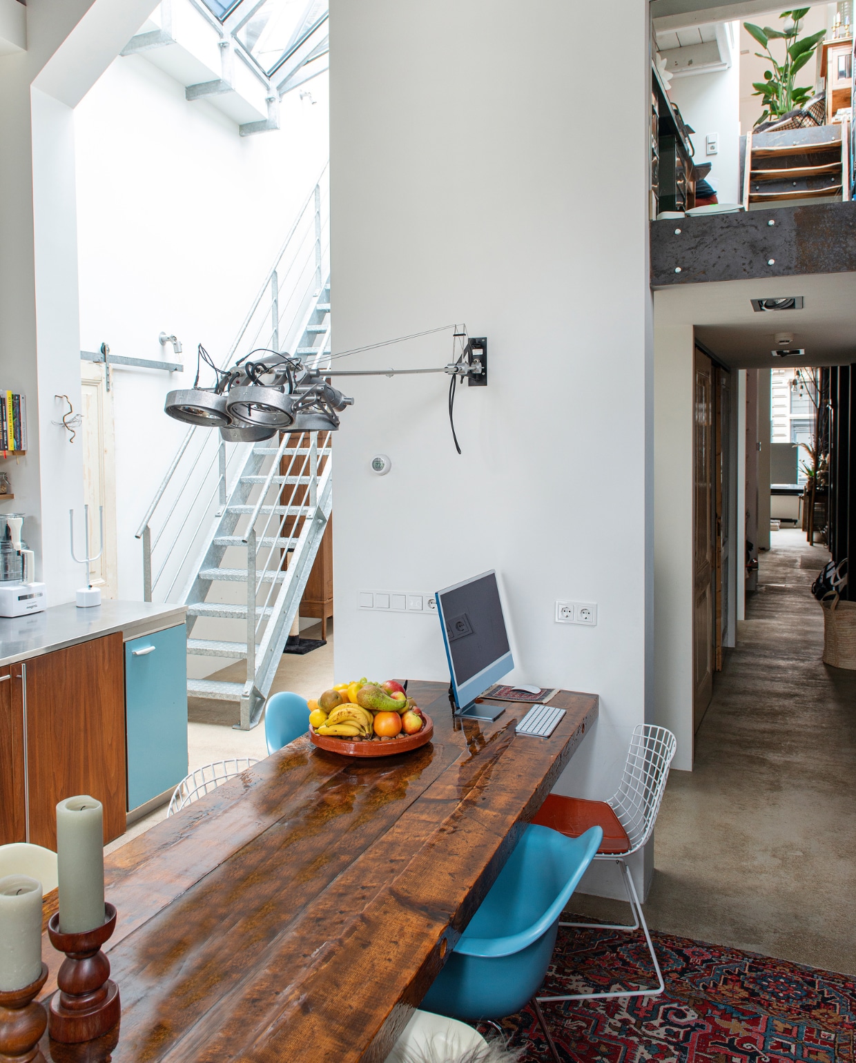 Tafel zelfgemaakt van oude balken en behandeld met epoxy, witte en blauwe stoelen stoel Eames Plastic Armchair van Vitra, stoel ijzerdraad Wire Chairs van Harry Bertoia voor Knoll, lampen boven tafel en in gang Nomad van Modular, Perzisch tapijt vintage, driearmige kandelaar Flames van Chris Kabel voor Droog, houten kandelaar en fruitschaal kringloopwinkel.