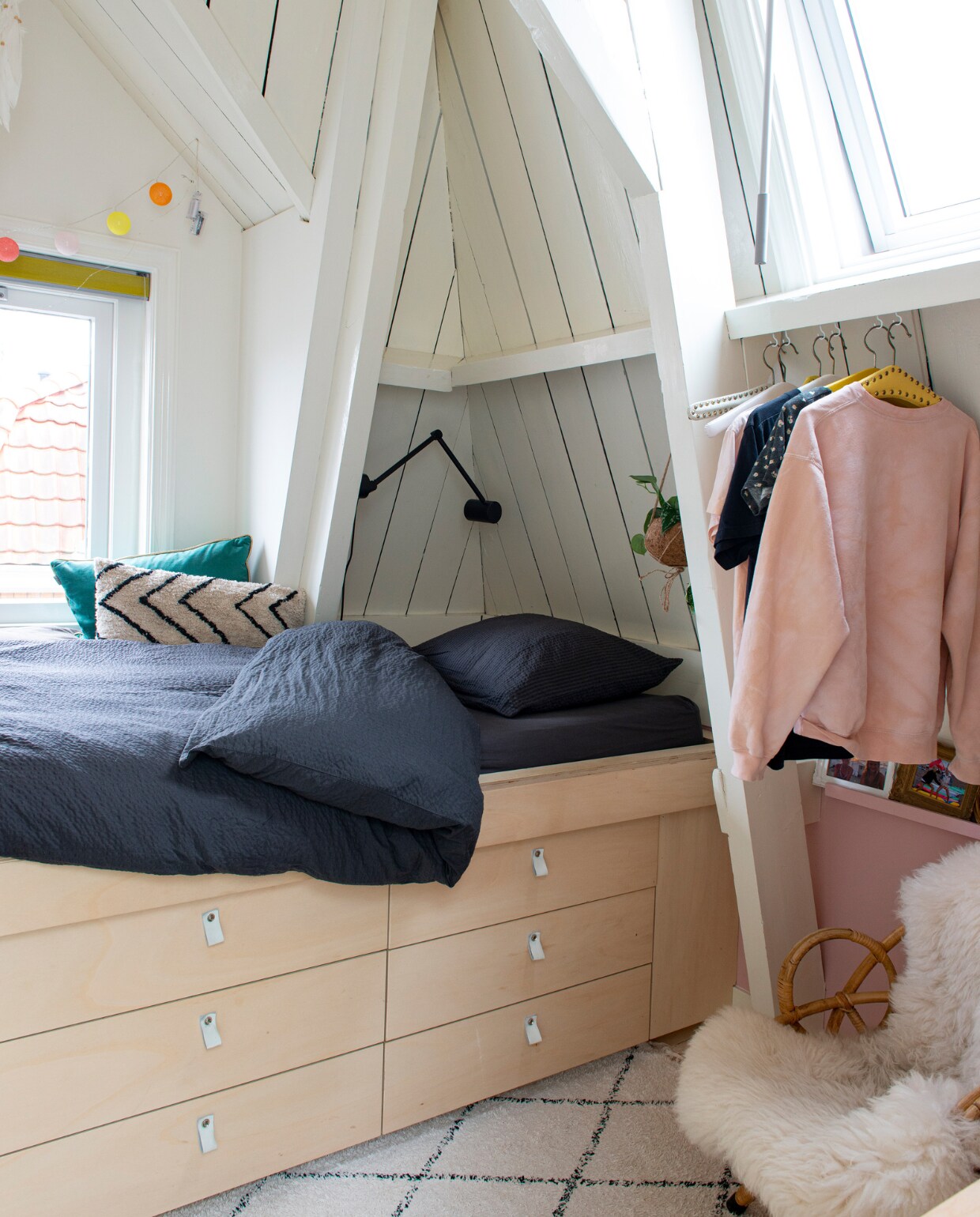 Zigzag kussen van HKliving, het bed heeft een basis van Ikea met zelfgemaakte fronten en leren handgreepjes, schapenvacht Polspotten, rotan stoel vintage, wandlamp Ikea, vloerkleed Søstrene Grene, blauw kussen Raaf, beddengoed Hema, lichtsnoer onbekend.