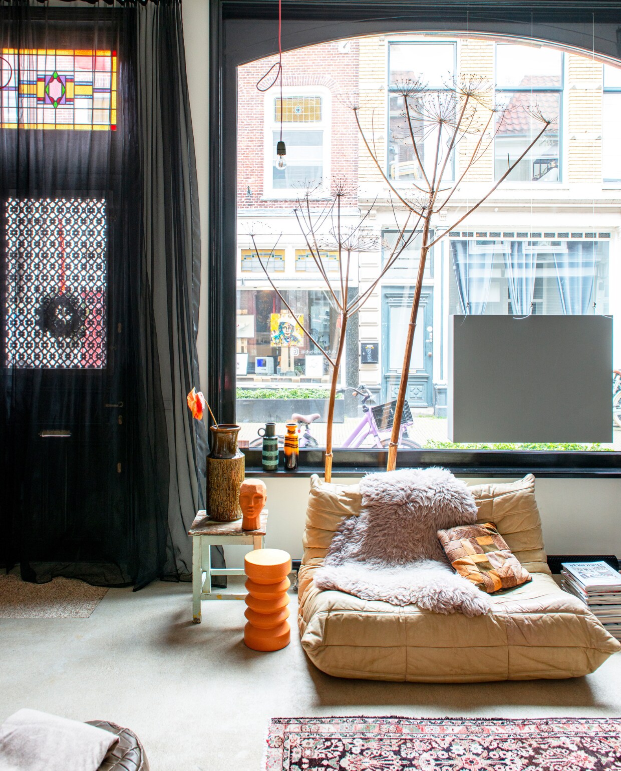 Oranje kruk en hoofd HKliving, houten kruk De Handelsfabriek, vintage fauteuil Togo van Ligne Roset via Marktplaats, schapenvacht Pols Potten, patchwork kussen rommelmarkt, vintage West-Germany-vazen via Sprinkel + Hop, stof deurgordijn en spankabel Ikea, hanglamp zelfgemaakt met materiaal van Sjakie’s, Perzisch tapijt kringloopwinkel.
