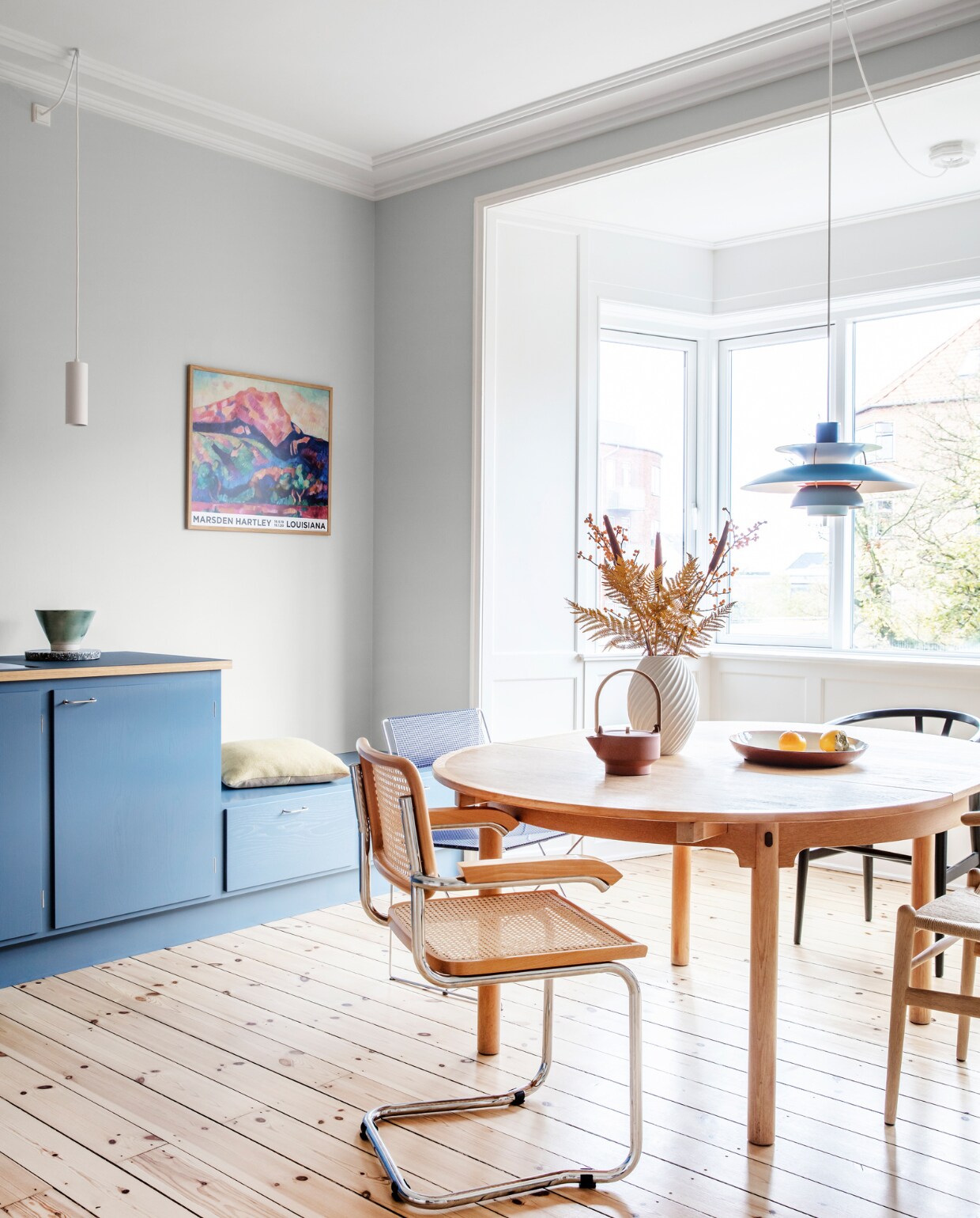 Muurverf Morgendis van Jotun. Keuken Stilleben Architects. Peper-en-zoutstel Hay. Tafel Øresund van Børge Mogensen. Vaas Morsø. Theepot Skagerrak og Stilleben. Stoelen Hans Wegner, Niels Jørgen Haugesen en Marcel Breuer. Originele houten vloer, gerestaureerd. Witte hanglamp Light-Point. Blauwe hanglamp PH 5 van Poul Henningsen. Kussen Hay. Overig herkomst onbekend.