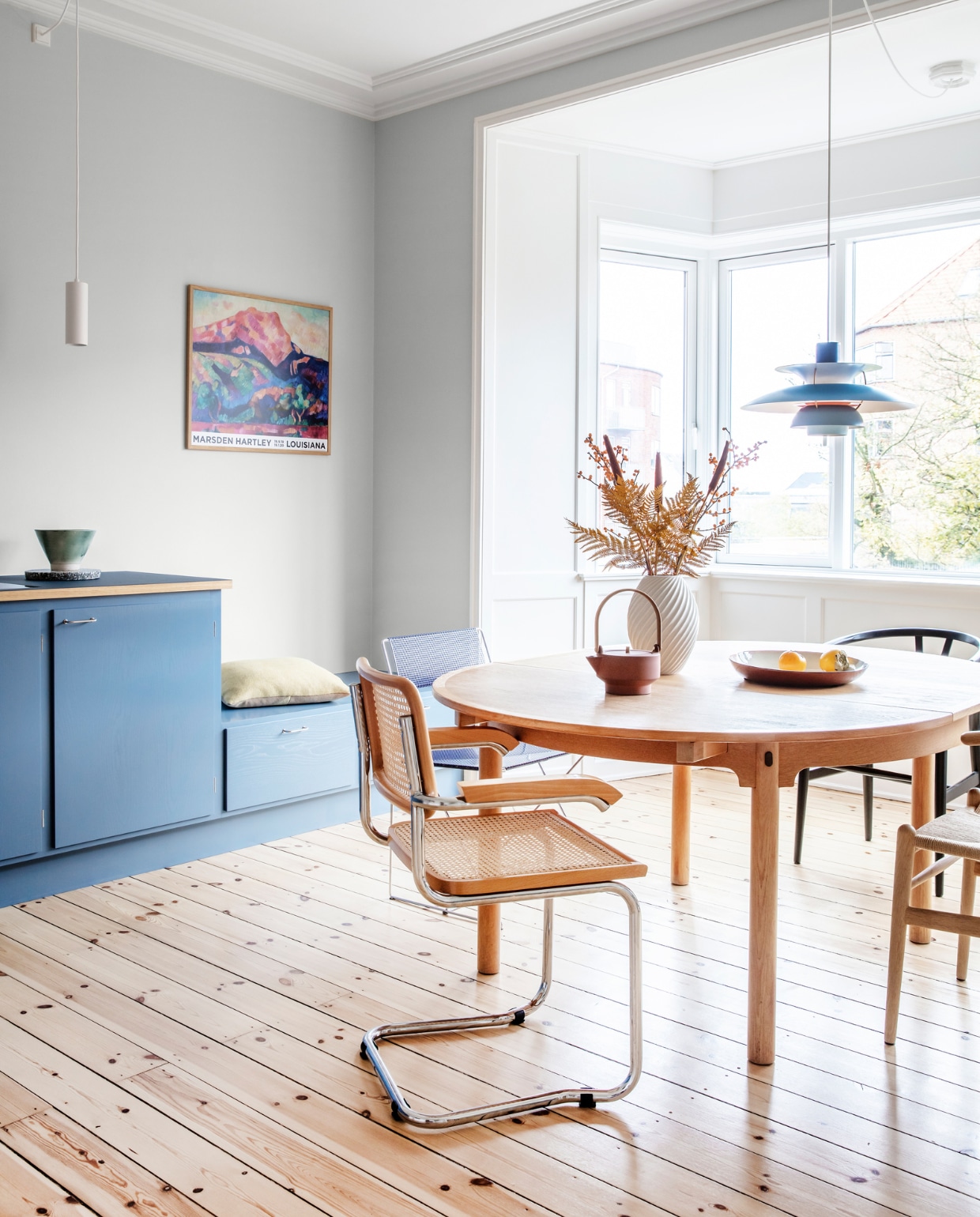 Muurverf Morgendis van Jotun. Keuken Stilleben Architects. Peper- en zoutstel Hay. Tafel Øresund van Børge Mogensen. Vaas Morsø. Theepot Skagerrak og Stilleben. Stoelen Hans Wegner, Niels Jørgen Haugesen en Marcel Breuer. Originele houten vloer, gerestaureerd. Witte hanglamp Light-Point. Blauwe hanglamp PH 5 van Poul Henningsen. Kussen Hay. Overig herkomst onbekend.