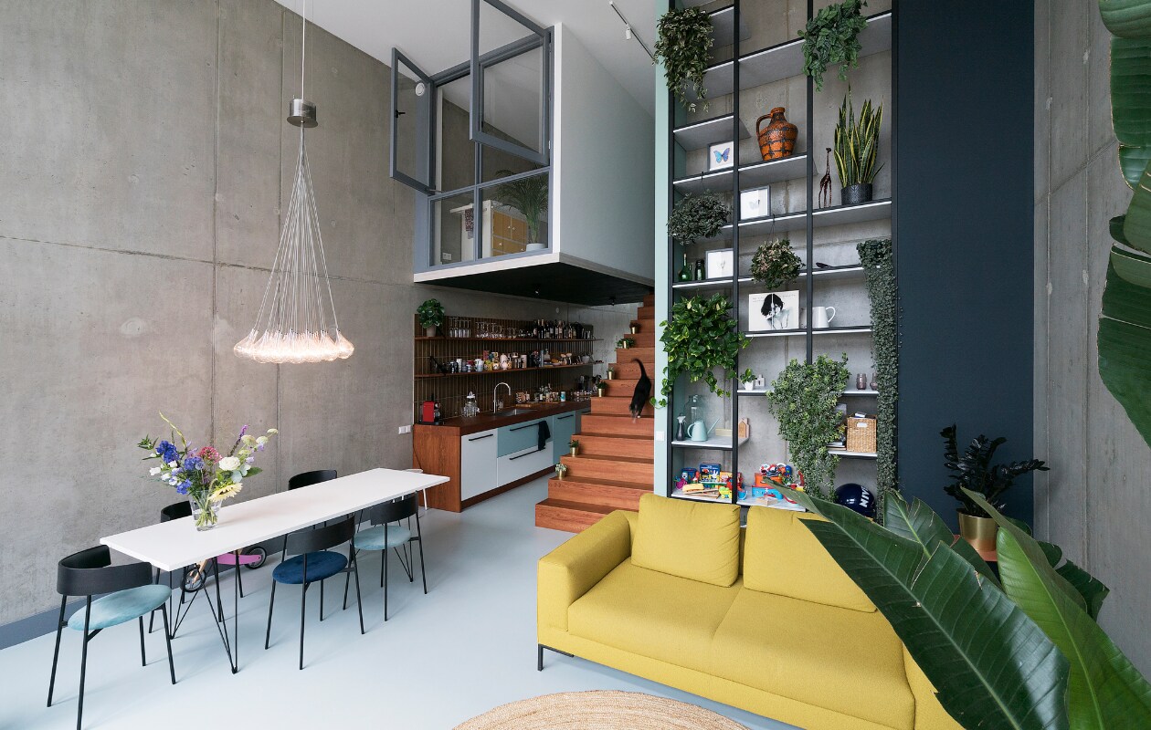 Bank Aikon Lounge van Design on Stock. Eetkamerstoelen Friday van Fest. Tafel Magis Tavolo XZ3 via Flinders. Maatwerkkeuken, eikenhouten trap en stalen kast ontwerp Martijn Frank Dirks, uitvoering Spinder Interieurbouw. Inbouwapparatuur Siemens. Downdraft afzuiger Wave Design. Tegels Ceramiche Grazia 6,6×26 cm in kleur Pepe. Vloer DGF polyurethaan PU Gietvloer in kleur NO.05.65 via Design Gietvloer Amsterdam. Betonnen muren geïmpregneerd met Hydrablock Pro voor matte look. Gouden bloempotten Ikea. Grijze verf Sikkens ACC Aqua Zijdeglans kleur SN.02.57. Donkerblauwe verf Sikkens ACC Aqua Zijdeglans kleur SO.10.20.