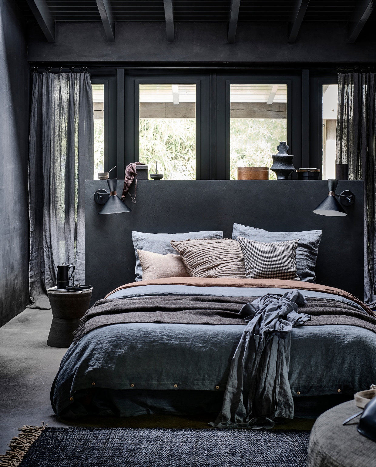 Matzwarte metalen wandlamp Hoodies, 25x25x50,5 cm (lxbxh) € 89,95 (ook verkrijgbaar in zandgrijs). M.m.v. bymolle.com (linnen laken in kleur Slate, linnen dekbedovertrek in kleur Slate en Cacao, linnen kussensloop in kleur Slate, linnen gordijnen in kleur Slate), letoile.store (vloerkleed, zwart houten bord, keramieken wierookhouder, beige linnen kussen), loods5.nl (keramieken bijzettafel, fauteuil), paviljoennoord.com (koffiepot, zwart-wit geruit kussen, leren tas), hm.com (plaid, bruin kussen, zwarte vaas, linnen ochtendjas), vtwonen.nl (houten mok van Serax). Overig privébezit.