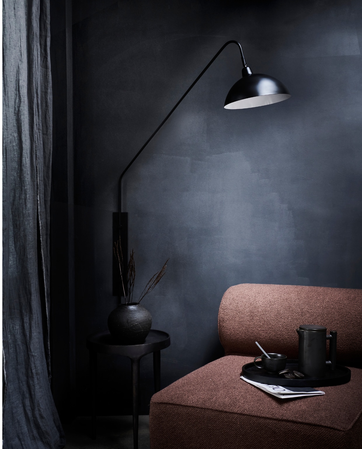 Matzwarte metalen wandlamp Orion, 127×110 cm (hxb), kap 30 cm (Ø) € 133,95.M.m.v designtales.nl (fauteuil, mok en theepot van Menu), loods5.nl/design (metalen bijzettafel), bymolle.com (linnen gordijn in kleur Slate), vtwonen.nl (dienblad van Serax), zarahome.com (zwarte bolvaas). Overig privébezit.