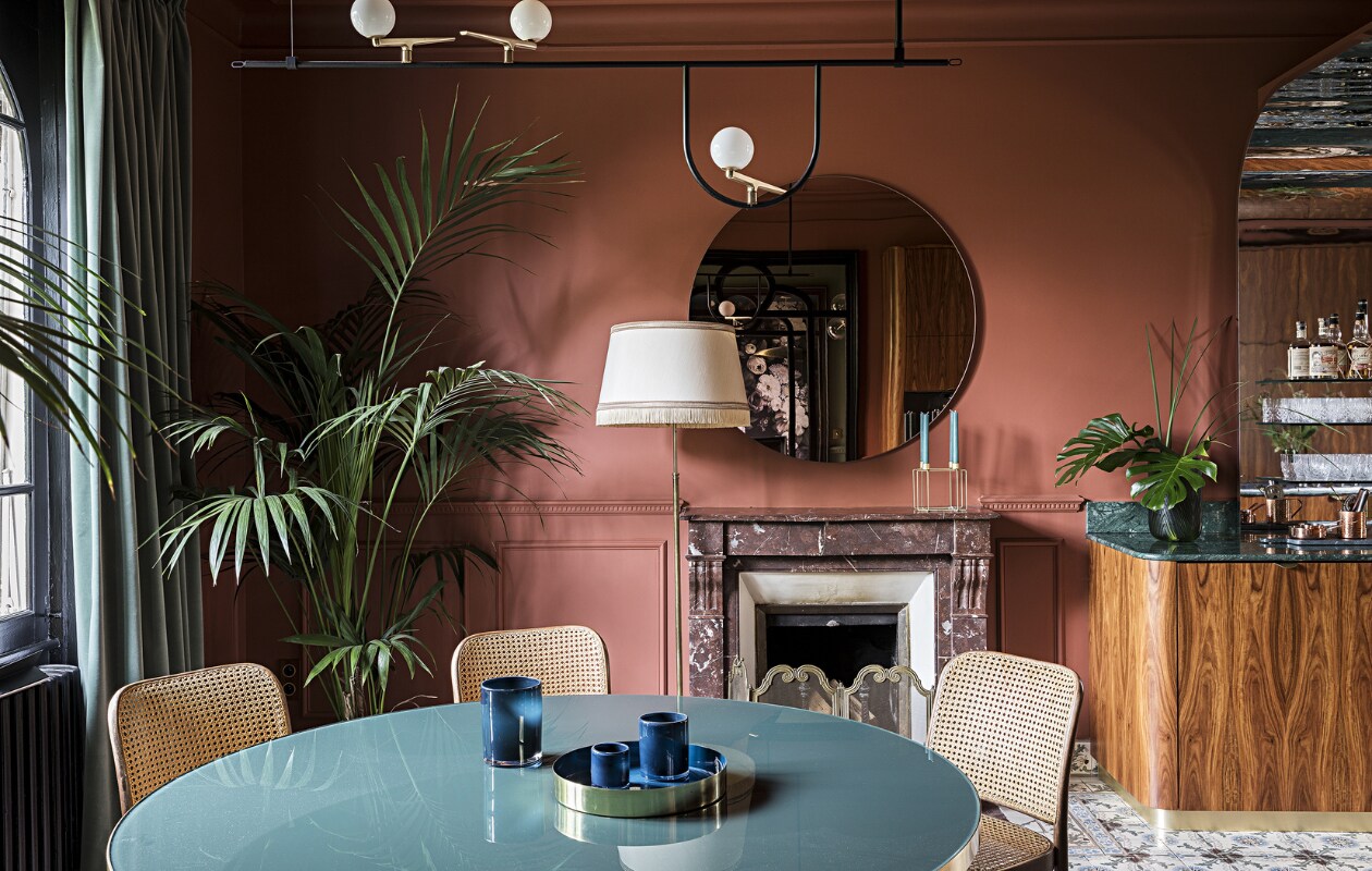Muurverf Book Room Red van Farrow &amp; Ball. Tafel Gubi. Stoelen en vloerlamp tweedehands. Hanglamp Yanzi Artemide. Spiegel AYTM. De schouw en cementtegels zaten al in het huis. Overig onbekend.
