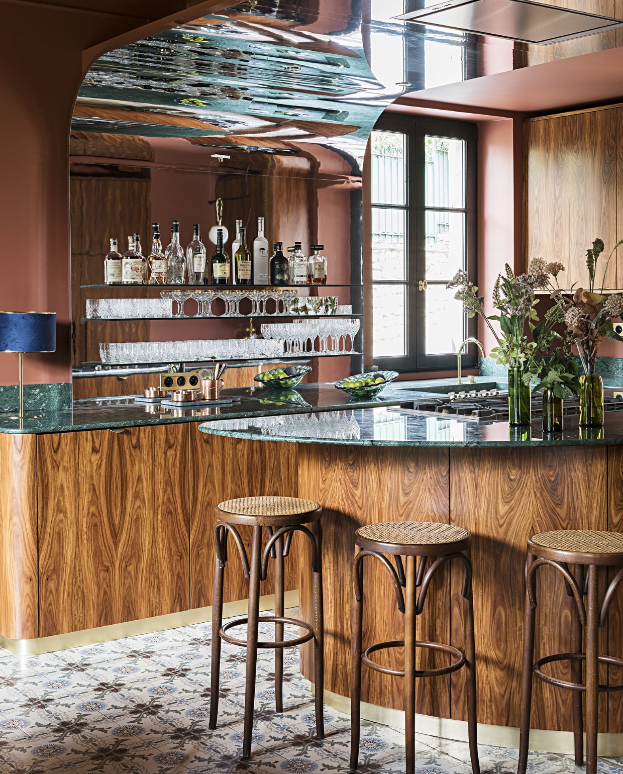 De keuken, ontworpen door Fanny en Fabrice zelf met interieurarchitect Carlos Pujol, is uitgevoerd in palissanderfineer en verde Guatamala (groen marmer). De achterwand is bekleed met spiegelfolie. Muurverf Book Room Red van Farrow &amp; Ball. Barkrukken tweedehands. Overig onbekend.