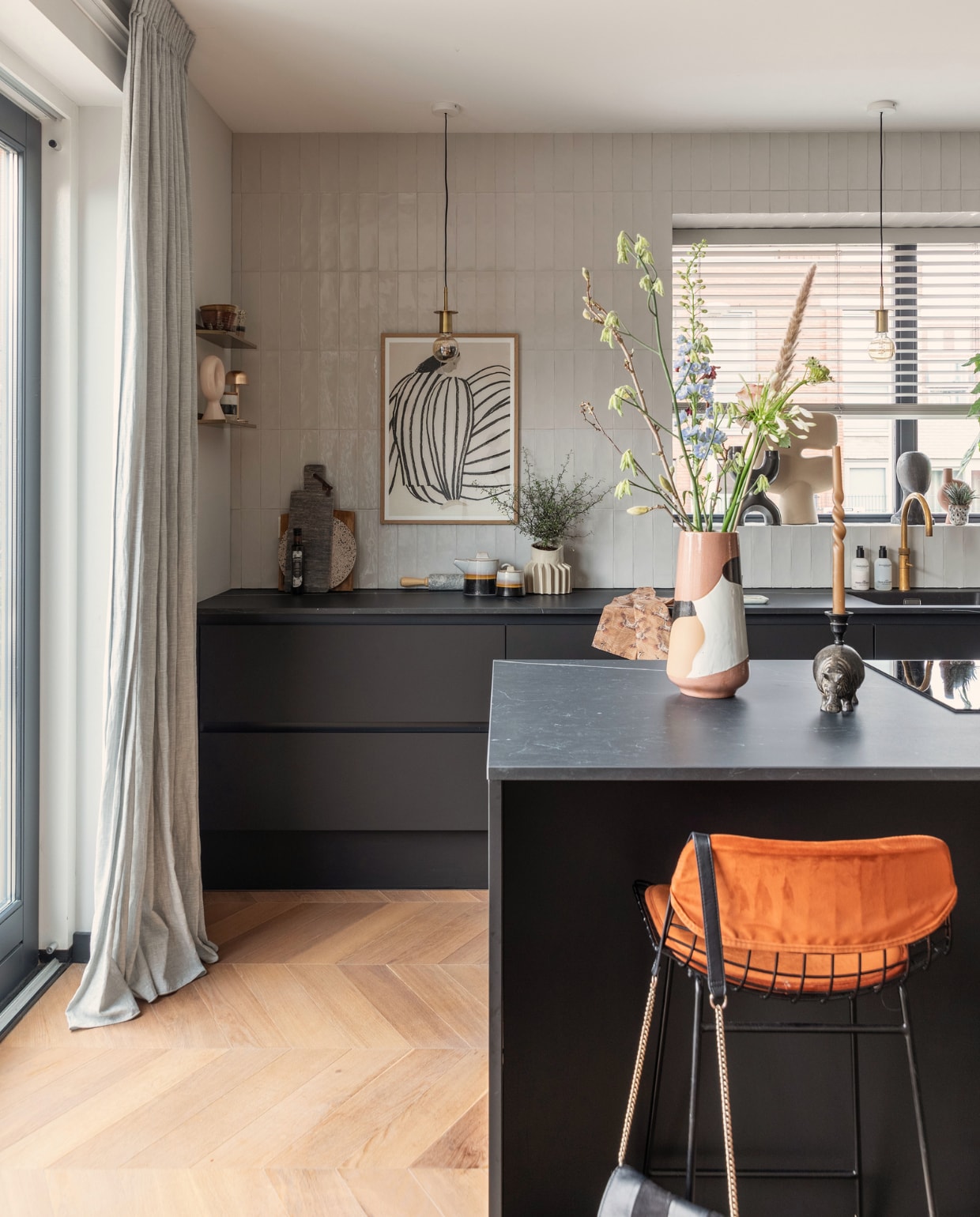Keuken Bruynzeel Keukens, vloer Beboparket, wandtegels Tegeldeal, gordijnen Kwantum, kunst The Poster Club. Vaas op eiland, servies op aanrecht en barkruk HKliving. Messing wandplanken House Doctor. Oplaadbare messing lamp Humble Lights. Grote vaas in vensterbank 101Copenhagen. Snijplanken Brood en Plank, vaas met ribbels Floris Wubben. Hanglampen Gekaapt. Overig onbekend.