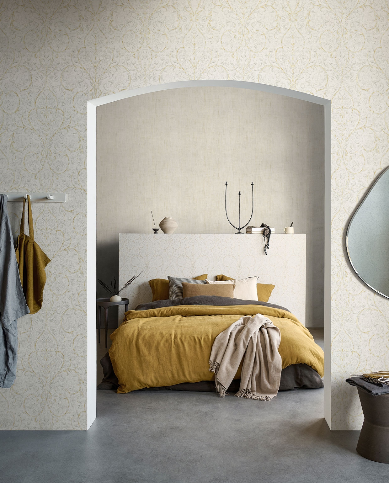 Behang op voorste wand en hoofdbord Classic Curl Light Grey, op achterste wand Linnen Gold, 53 cm breed, rol van 10 meter €29,99 (Classic Curl ook verkrijgbaar in Sea Green).M.m.v. pure-original.nl (muurverf Fresco in kleur Old Flax), paviljoennoord.com (linnen ochtendjas, linnen tas, linnen dekbedovertrekken, linnen kussenslopen, zwart wit geruit kussen, olijfgroen kussen), vtwonen.nl (spiegel van Ferm Living), loods5.nl (stenen kruk, metalen bijzettafel), letoile.store (keramieken vaasje, wierookhouder, mok), hm.com (gedraaide vaas), sissy-boy.com (metalen kandelaar, plaid), zarahome.com (wit kussen). Overig privébezit.