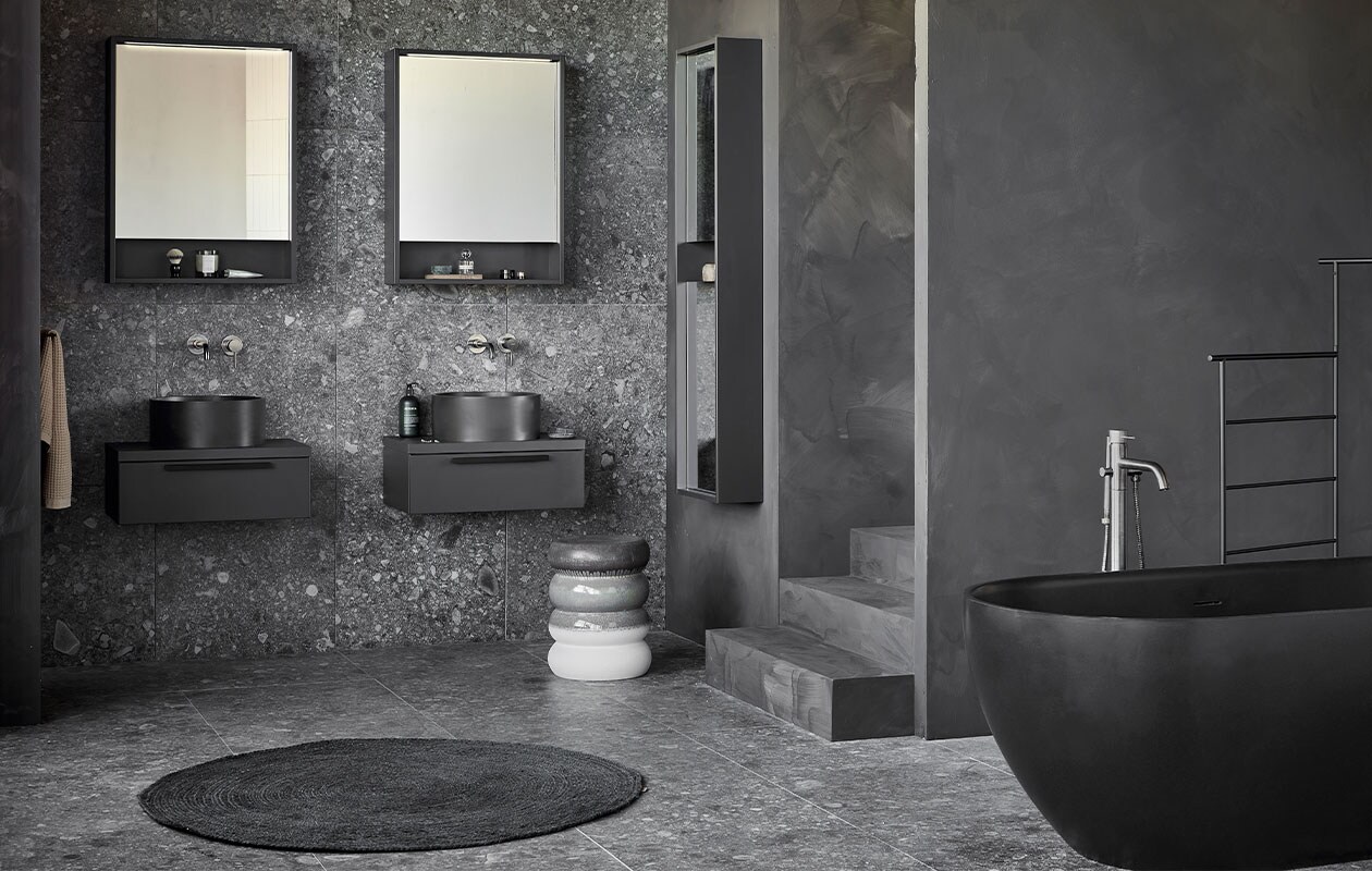 Kunststof spiegelkasten Handy Beauty in zwart, inclusief ledstrip met bewegingssensor, 59,6x60x10 cm (lxbxd)per stuk (ook verkrijgbaar in breedtematen 90 cm en 120 cm en in wit, zand en grijs). Quartz waskommen Circle in zwart, 37×15 cm (Øxh) per stuk (ook verkrijgbaar in grijs en in Top Solid en Marmer). Kunststof afdekblad in matzwart, 60 cm . Kunststof onderkasten Tidy in matzwart, 1 lade met handgreep, 20x60x40 cm (lxbxd)  per stuk. Spiegelkolomkast Handy Beauty Long in matzwart met 2 dubbelzijdige spiegeldeuren, 150x40x16 cm (lxbxd) (ook verkrijgbaar in wit, zand en grijs). Quartz bad Endless in zwart, 160x73x57 cm (lxbxh), inhoud 200 liter,  (ook verkrijgbaar in grijs en in Top Solid in de kleur zand). Op de wand en vloer vtwonen tegels Composite Black antracite, 60×60 cm, -.M.m.v. vestingh.nl (kleur op de muur Night Sky No.101), zarahome.com (handdoek, geurkaars in glas), vtwonen.nl (rond juten vloerkleed Eternal van Ferm Living, wandlampen Cast Sconce van Menu, zwart kledingrek Dora van Ferm Living, kruk Bulb van vtwonen), nordal.eu (groen marmeren schaaltje), stories.com (tube crème, oorbellen), wonenmetlef.nl (bruine onderzetter Merge van Ferm Living). Overig privébezit.